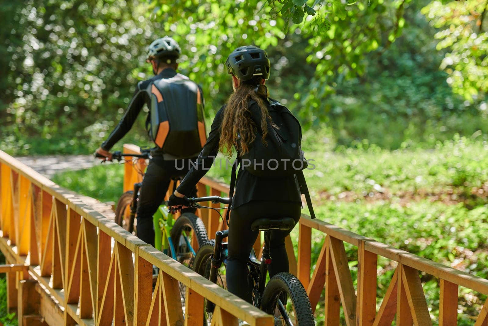 A blissful couple, adorned in professional cycling gear, enjoys a romantic bicycle ride through a park, surrounded by modern natural attractions, radiating love and happiness by dotshock