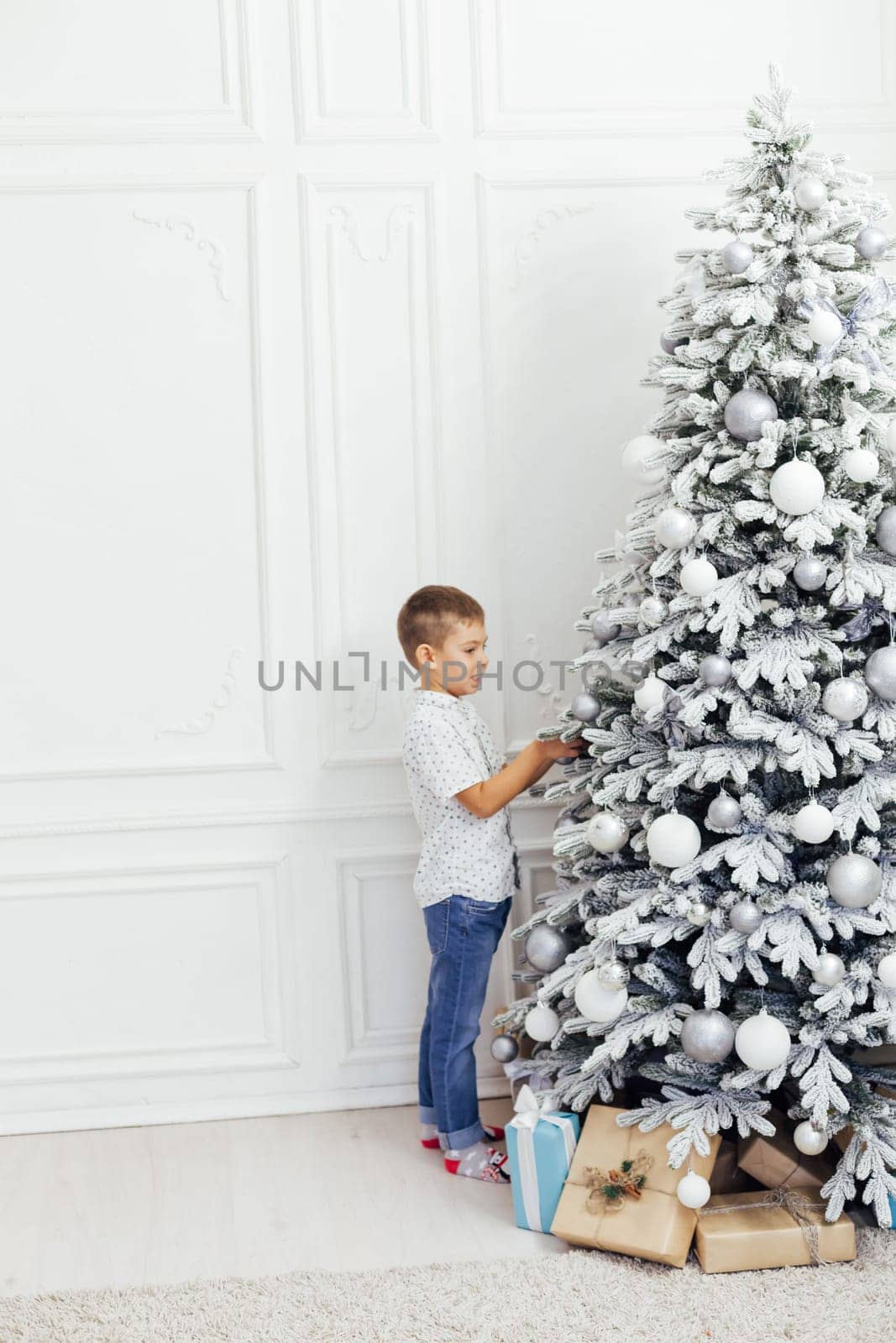 son decorates white Christmas tree with new year gifts