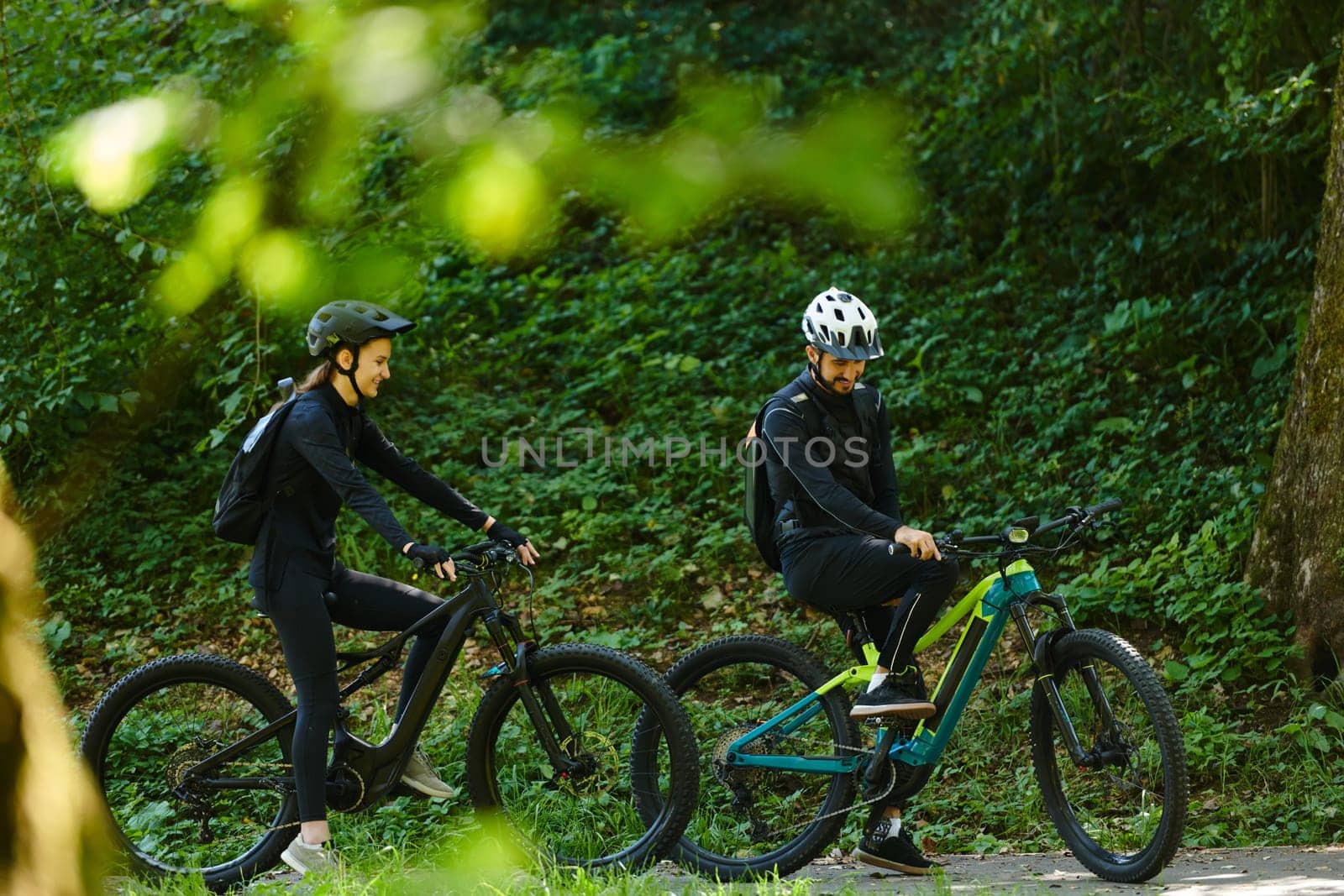 A blissful couple, adorned in professional cycling gear, enjoys a romantic bicycle ride through a park, surrounded by modern natural attractions, radiating love and happiness.