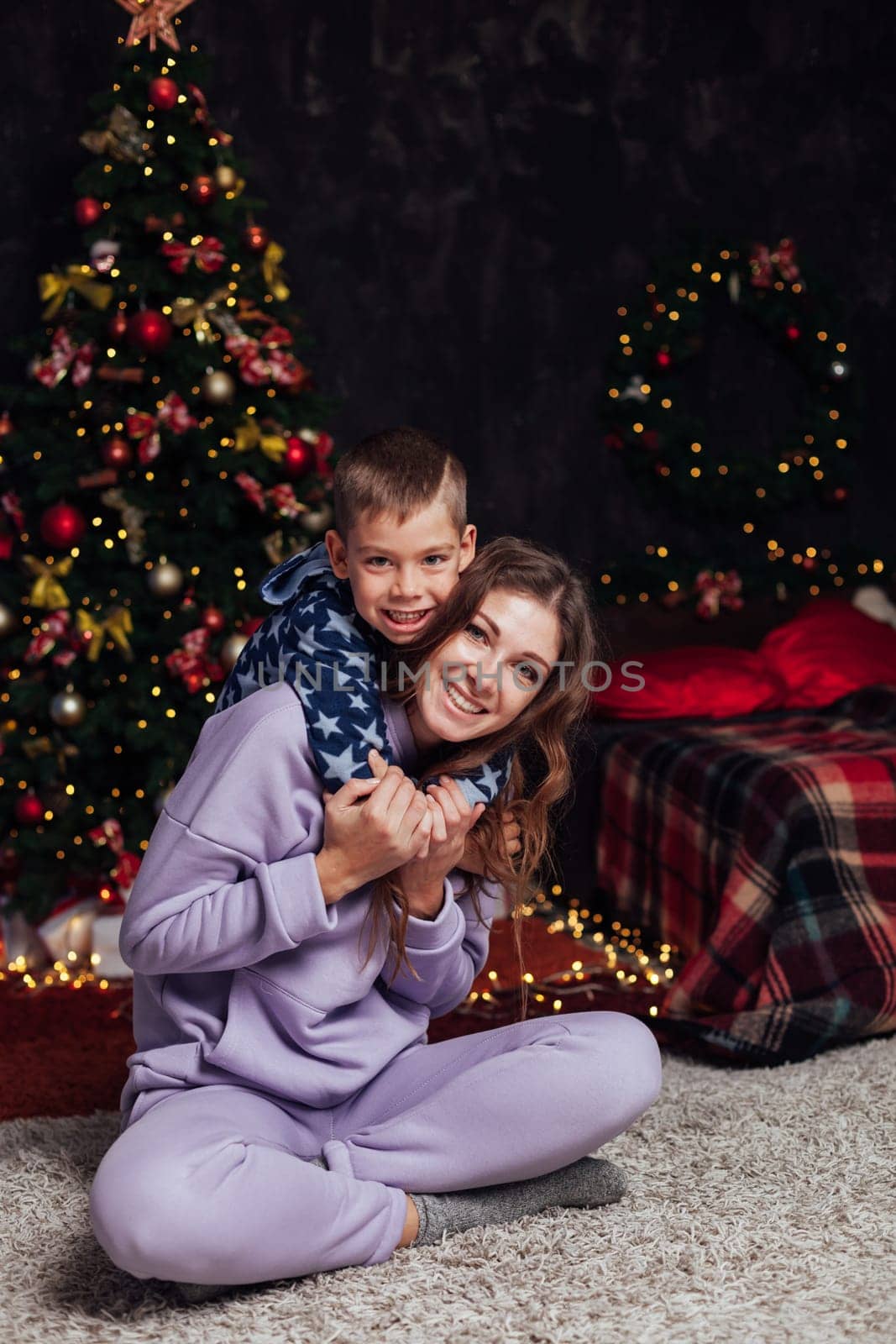 woman with son decorates white Christmas tree with new year gifts