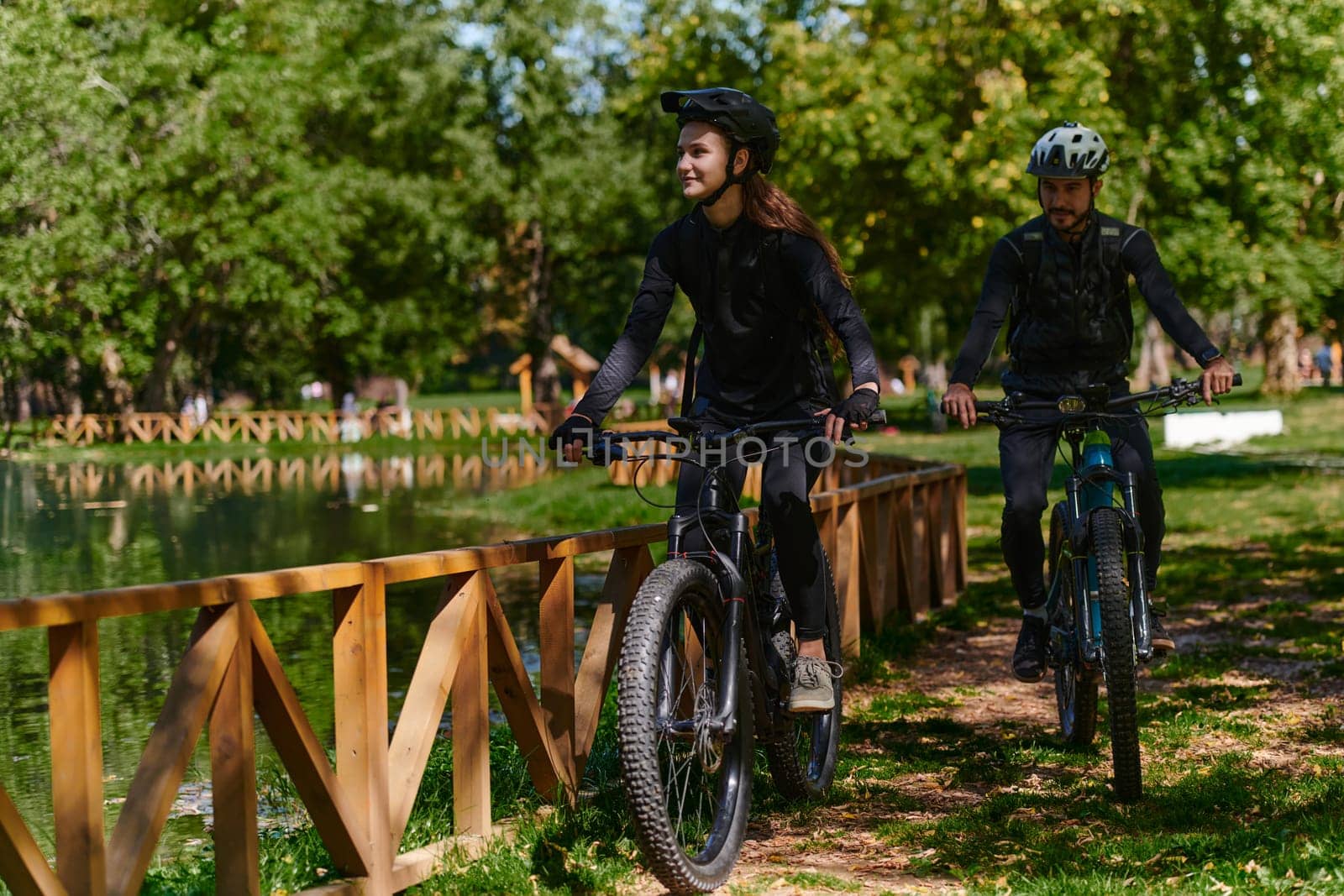 A blissful couple, adorned in professional cycling gear, enjoys a romantic bicycle ride through a park, surrounded by modern natural attractions, radiating love and happiness.