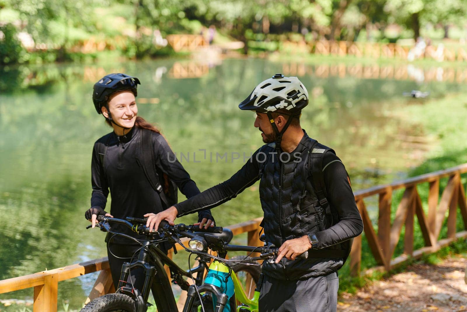 A blissful couple, adorned in professional cycling gear, enjoys a romantic bicycle ride through a park, surrounded by modern natural attractions, radiating love and happiness.