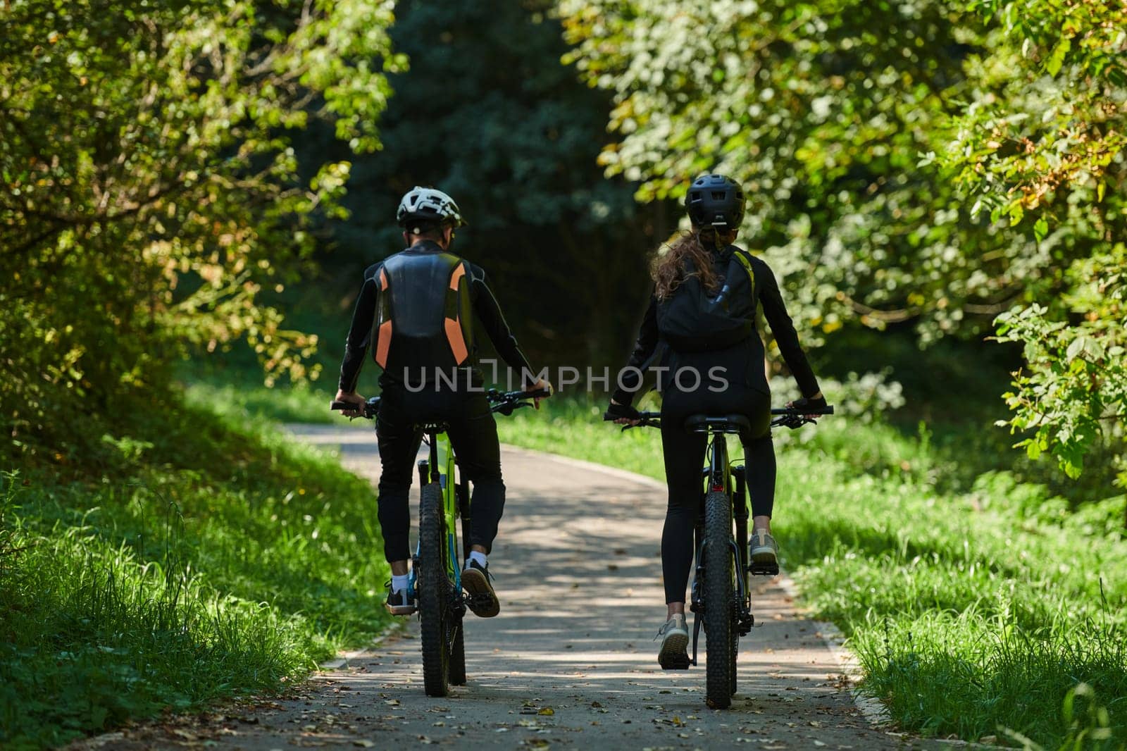 A blissful couple, adorned in professional cycling gear, enjoys a romantic bicycle ride through a park, surrounded by modern natural attractions, radiating love and happiness.