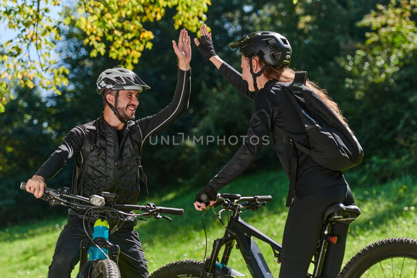 A sweet couple, adorned in cycling gear, rides their bicycles, their hands interlocked in a romantic embrace, capturing the essence of love, adventure, and joy on a sunlit path by dotshock
