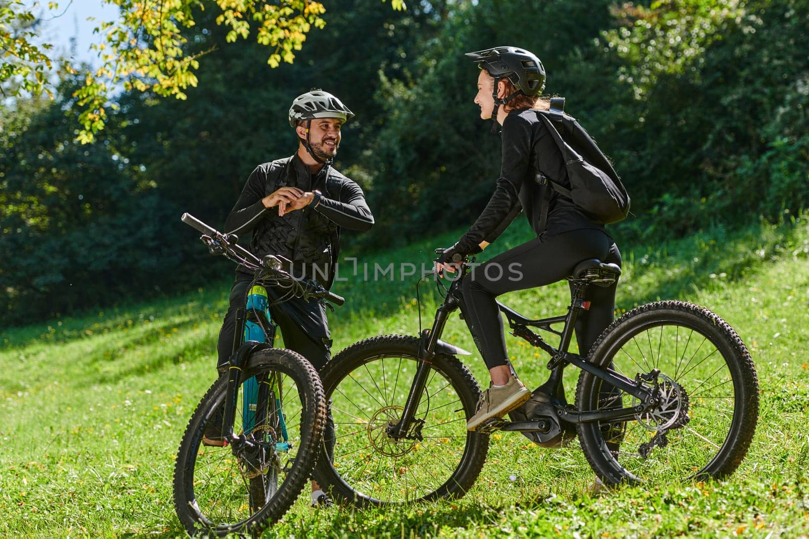 A sweet couple, equipped with bicycles and engrossed in coordinating their journey, checks their GPS mobile and watches while planning scenic routes in the park, seamlessly blending technology and outdoor adventure for a delightful cycling experience by dotshock