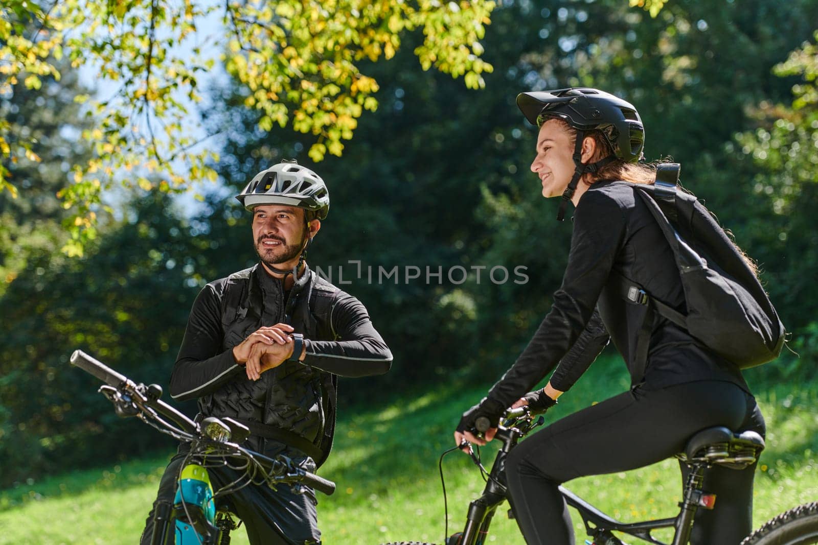 A sweet couple, equipped with bicycles and engrossed in coordinating their journey, checks their GPS mobile and watches while planning scenic routes in the park, seamlessly blending technology and outdoor adventure for a delightful cycling experience by dotshock