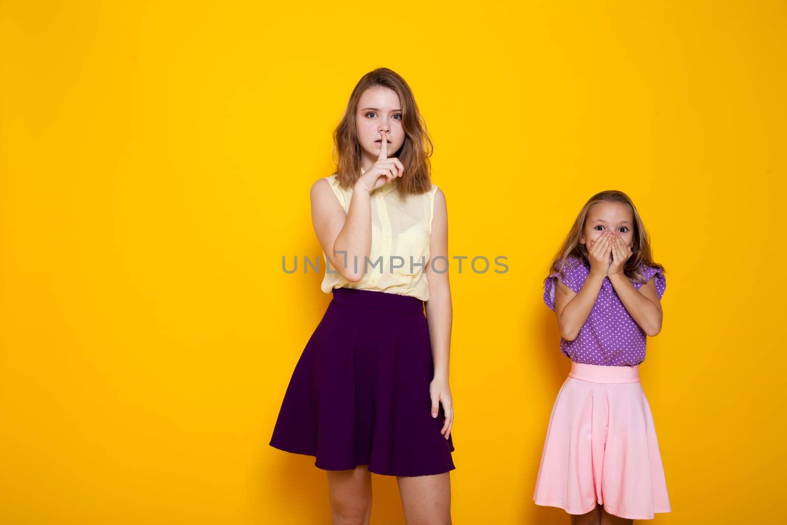 two girls are closing the mouth to make it quiet