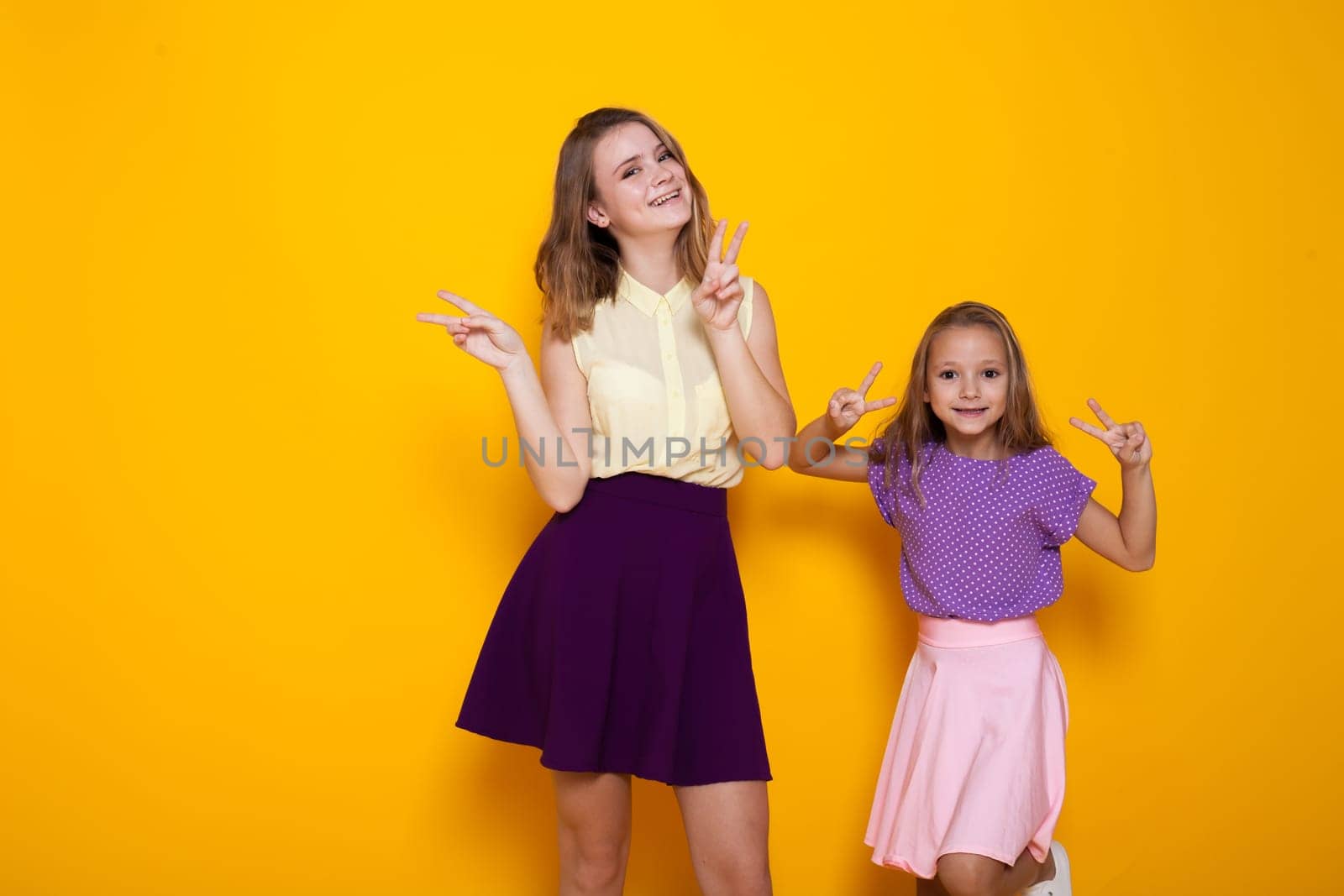 two girls in colored dresses laugh show fingers 1