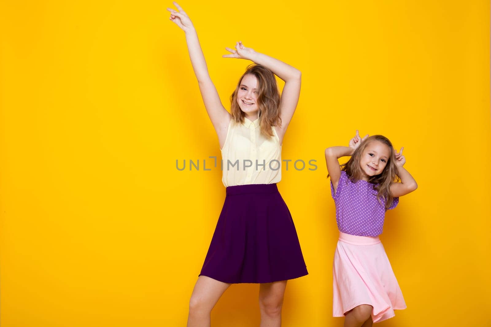 two girls in colored dresses laugh show fingers by Simakov