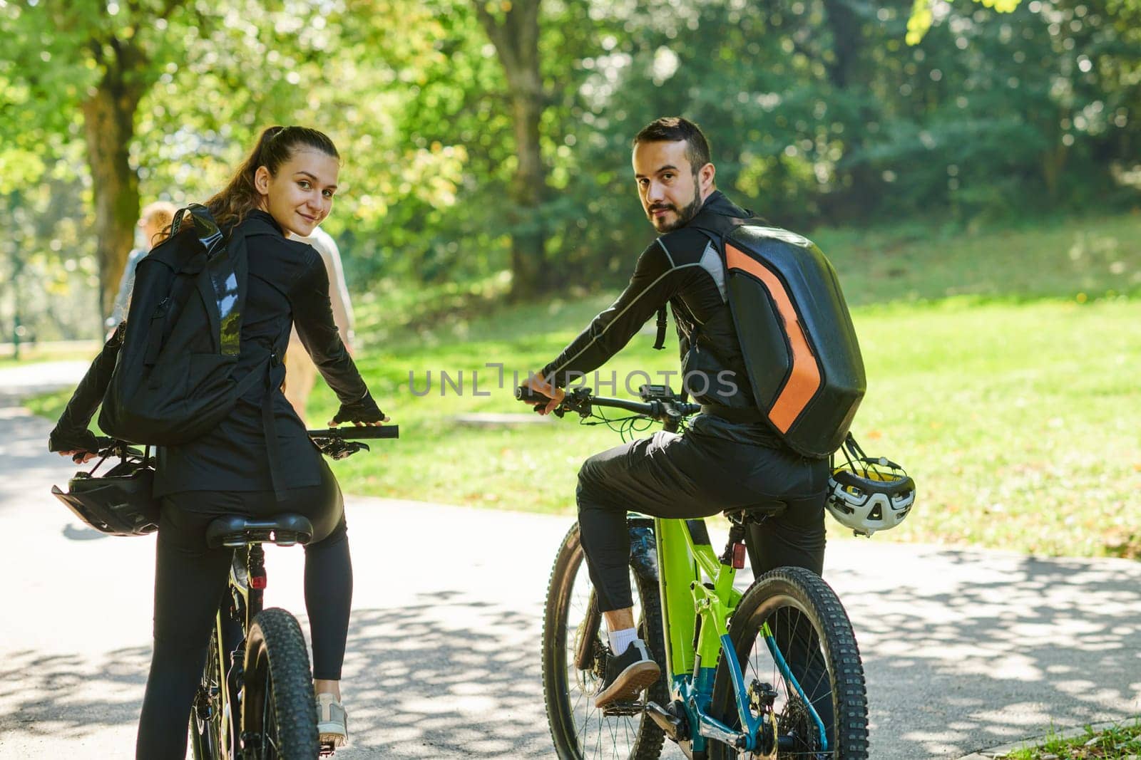 A blissful couple, adorned in professional cycling gear, enjoys a romantic bicycle ride through a park, surrounded by modern natural attractions, radiating love and happiness by dotshock