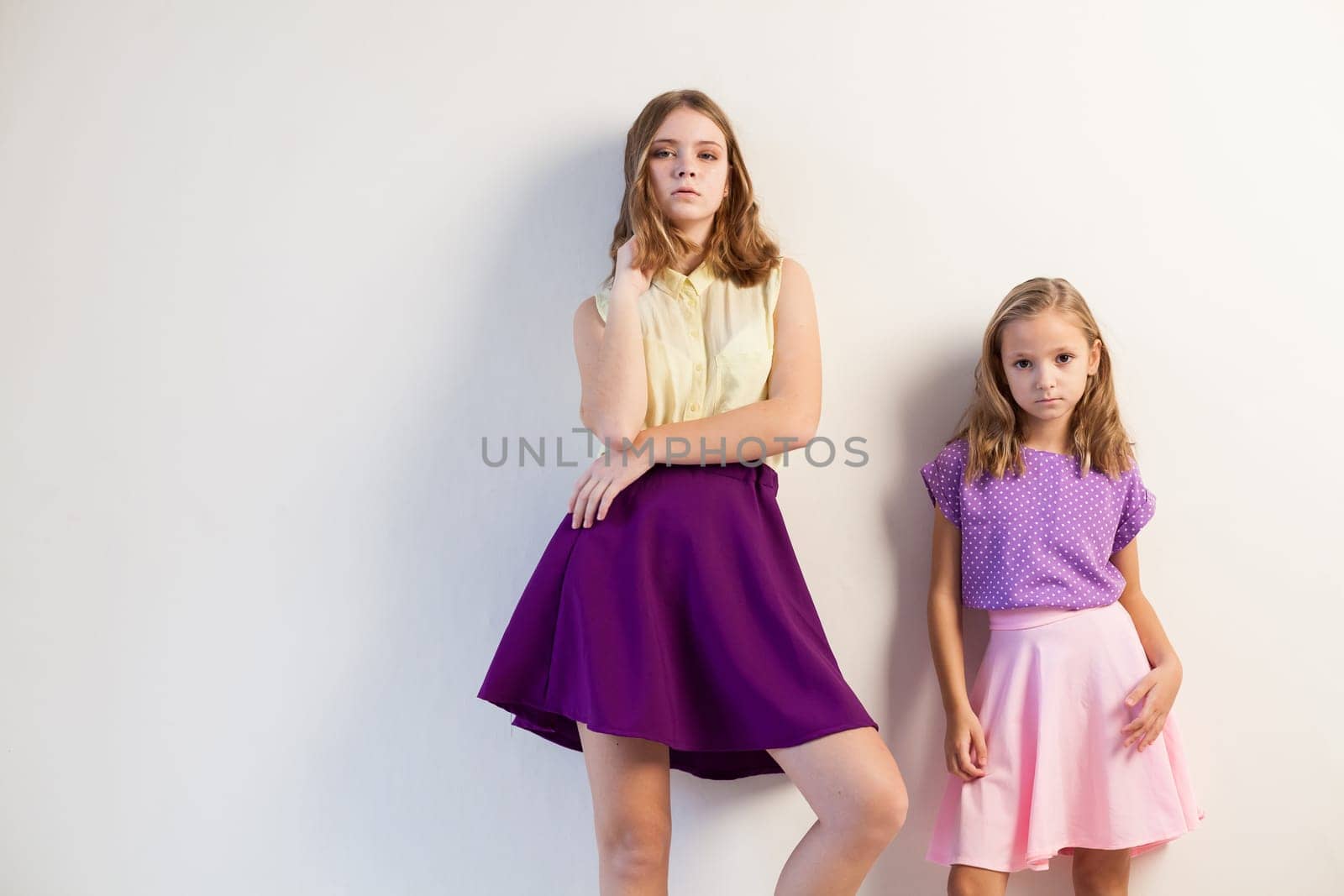 two sisters girls in colored dresses white walls 1