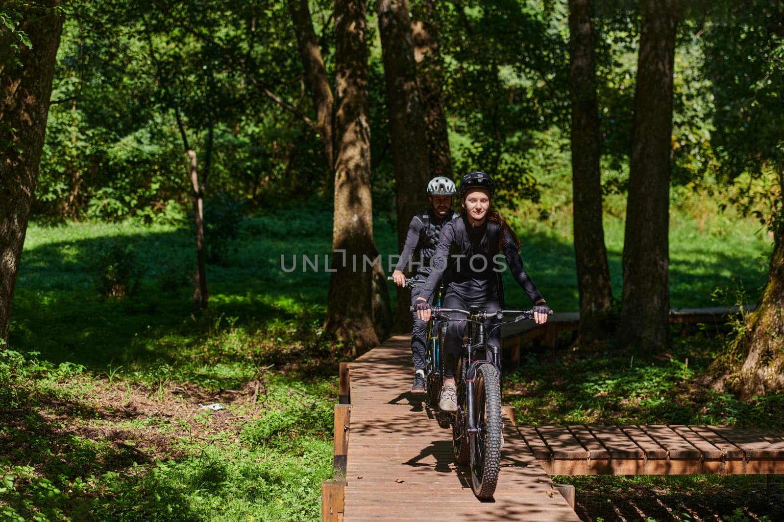 A blissful couple, adorned in professional cycling gear, enjoys a romantic bicycle ride through a park, surrounded by modern natural attractions, radiating love and happiness by dotshock