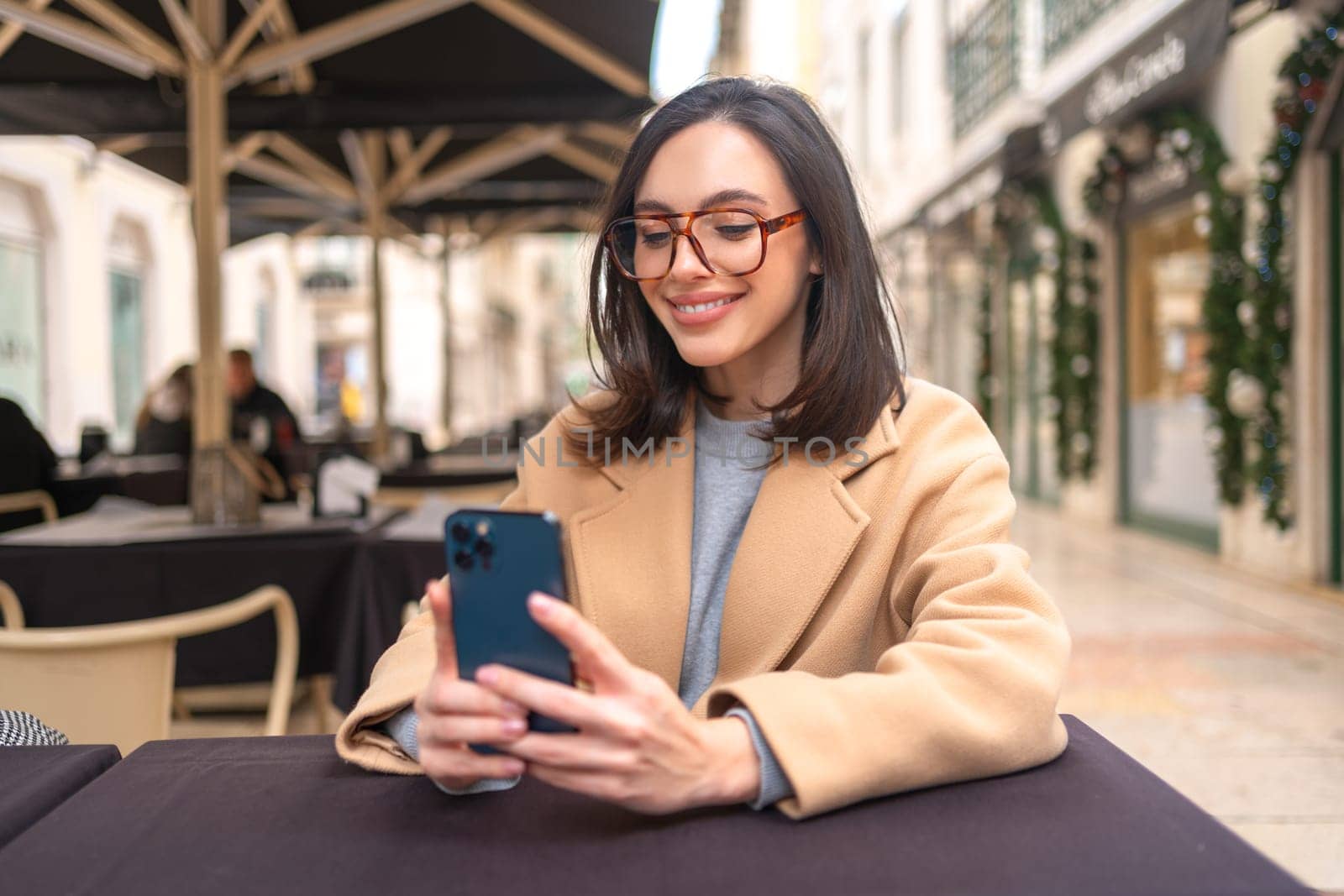 Smiling woman wear glasses sits in cafe takes selfies with phone by andreonegin