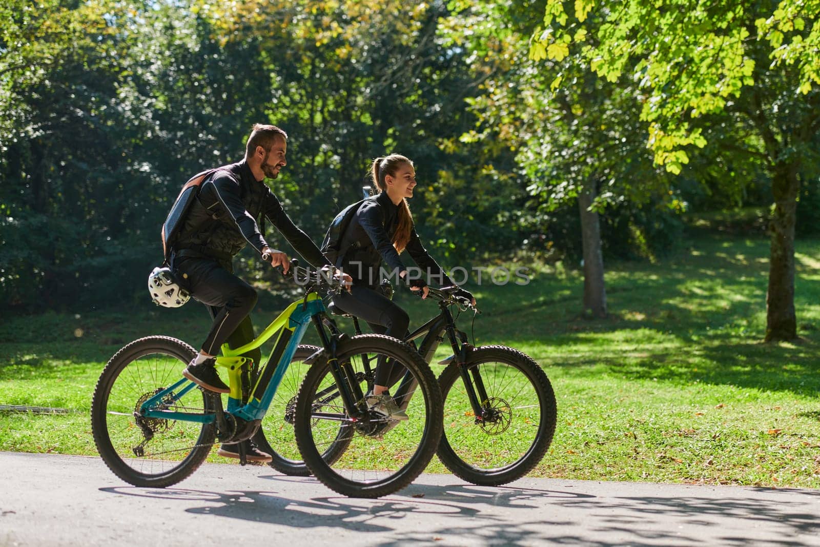 A blissful couple, adorned in professional cycling gear, enjoys a romantic bicycle ride through a park, surrounded by modern natural attractions, radiating love and happiness by dotshock