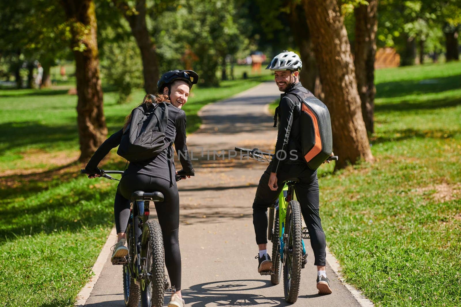 A blissful couple, adorned in professional cycling gear, enjoys a romantic bicycle ride through a park, surrounded by modern natural attractions, radiating love and happiness by dotshock