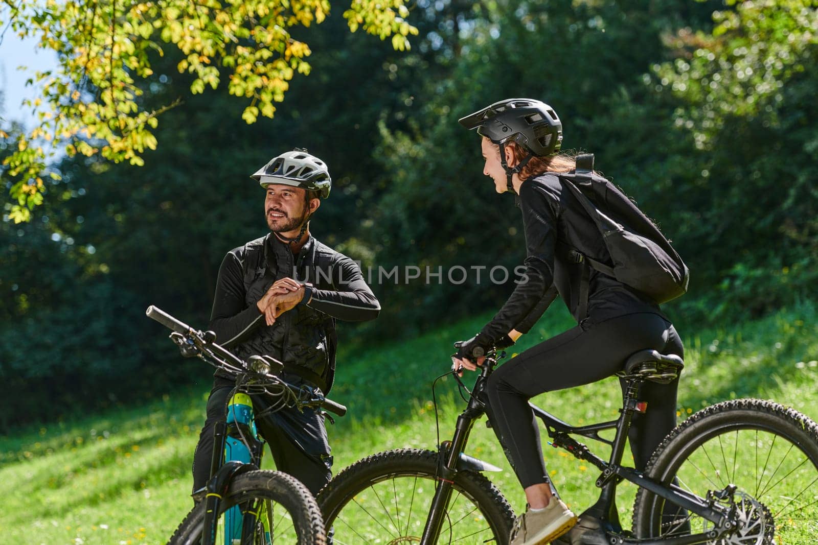 A sweet couple, equipped with bicycles and engrossed in coordinating their journey, checks their GPS mobile and watches while planning scenic routes in the park, seamlessly blending technology and outdoor adventure for a delightful cycling experience by dotshock