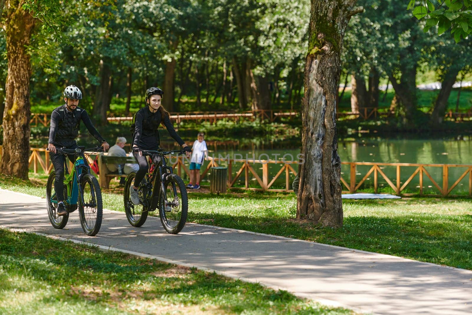 A blissful couple, adorned in professional cycling gear, enjoys a romantic bicycle ride through a park, surrounded by modern natural attractions, radiating love and happiness by dotshock