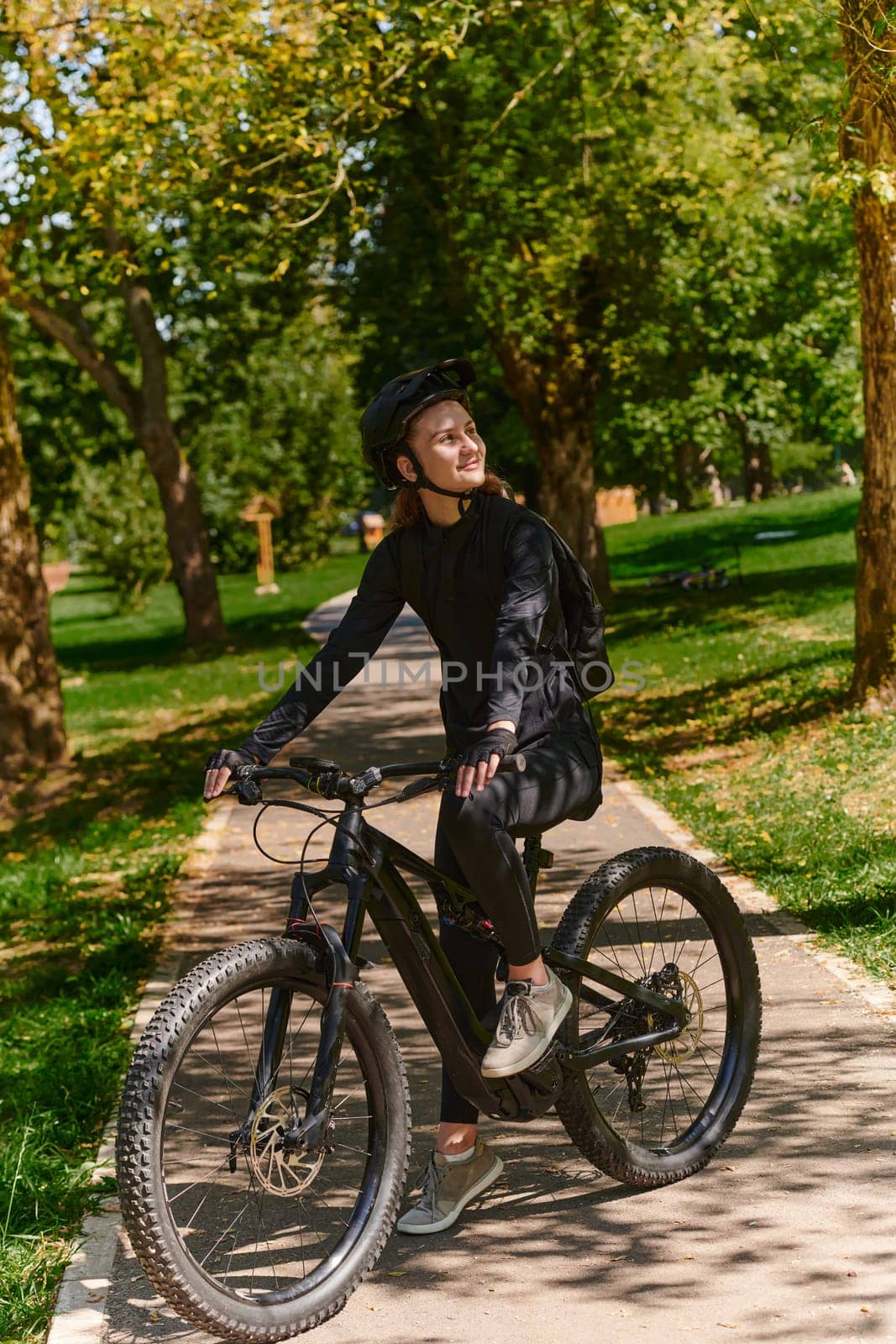 In the radiant embrace of a sunny day, a modern woman revels in the joy of cycling, her sleek bicycle and professional gear complementing her active lifestyle as she rides through the park, epitomizing a perfect blend of style and outdoor vitality.