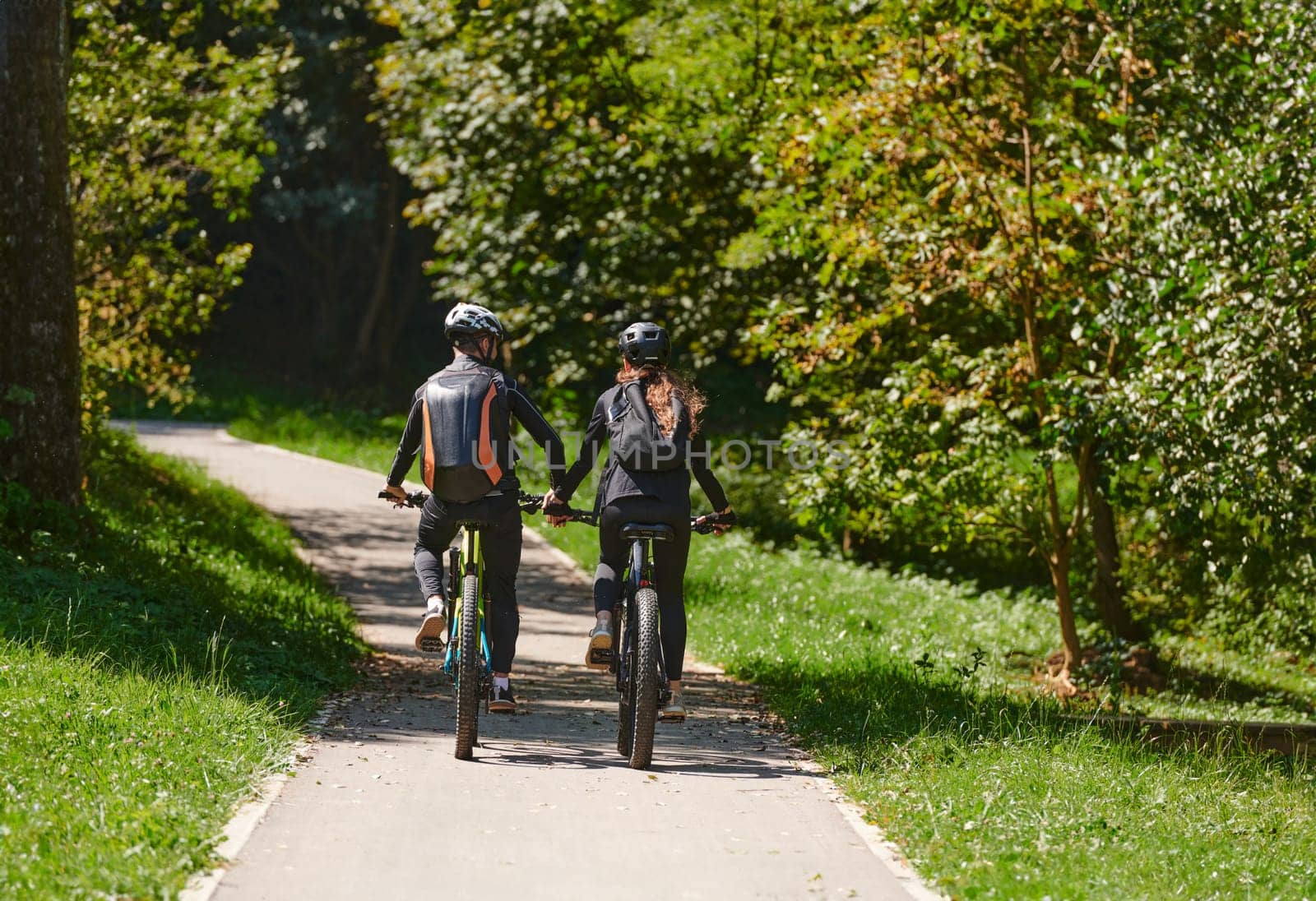 A blissful couple, adorned in professional cycling gear, enjoys a romantic bicycle ride through a park, surrounded by modern natural attractions, radiating love and happiness.