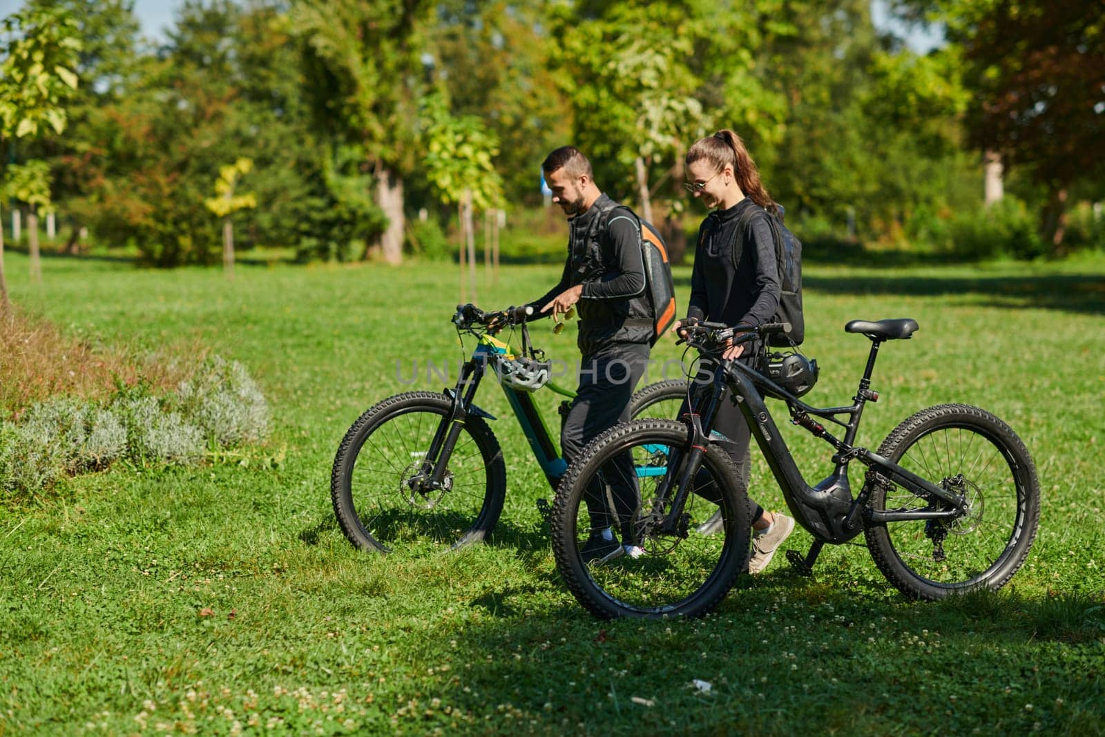 A blissful couple, adorned in professional cycling gear, enjoys a romantic bicycle ride through a park, surrounded by modern natural attractions, radiating love and happiness.