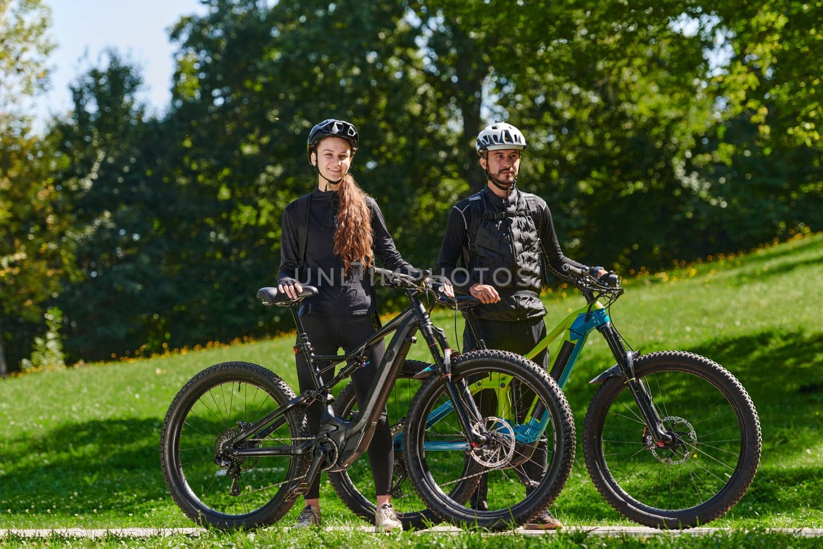 A sweet couple, equipped with bicycles and engrossed in coordinating their journey, checks their GPS mobile and watches while planning scenic routes in the park, seamlessly blending technology and outdoor adventure for a delightful cycling experience by dotshock