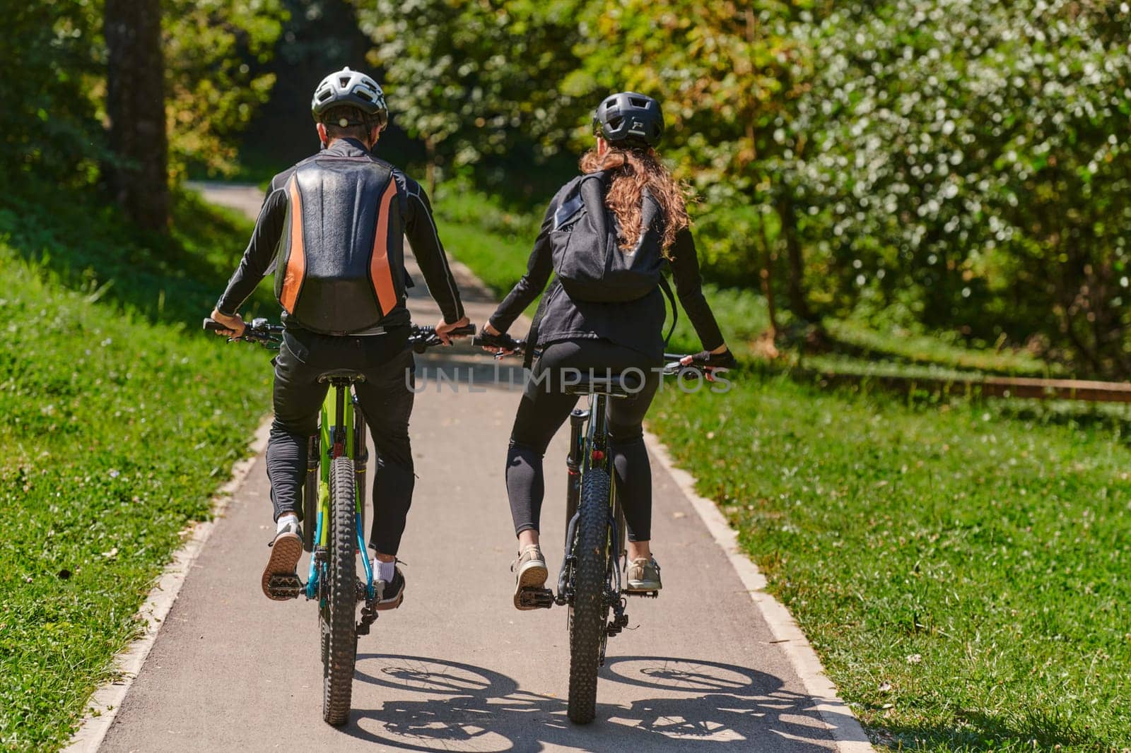 A blissful couple, adorned in professional cycling gear, enjoys a romantic bicycle ride through a park, surrounded by modern natural attractions, radiating love and happiness.