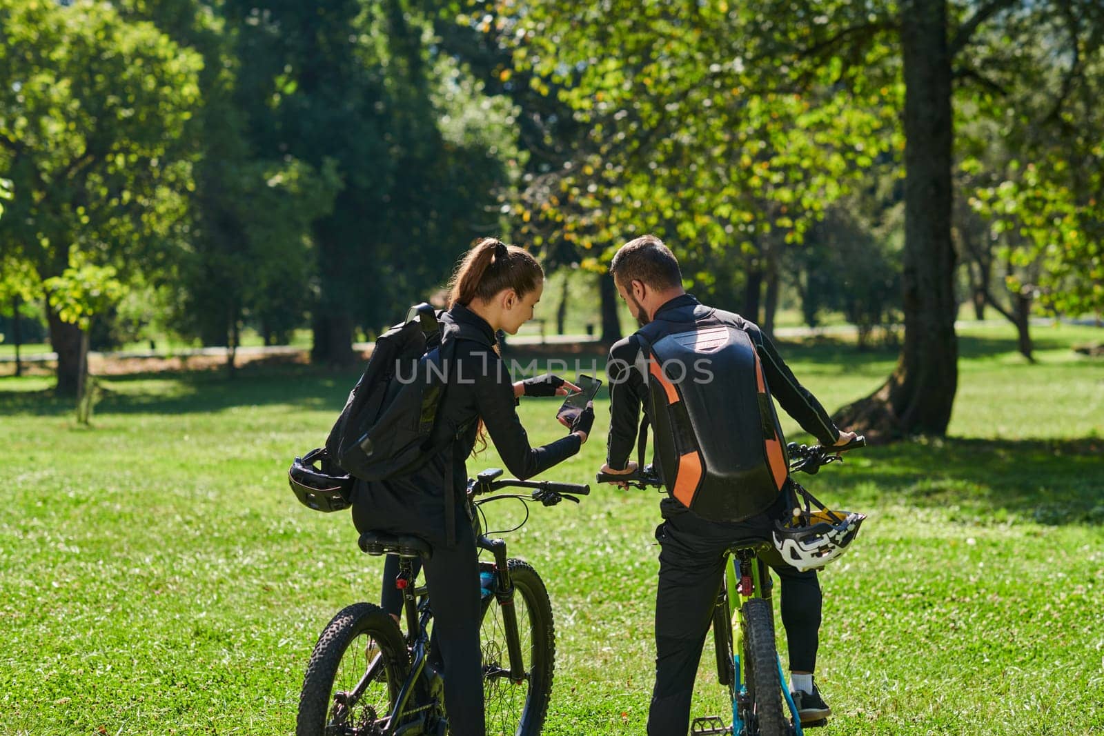 A blissful couple, adorned in professional cycling gear, enjoys a romantic bicycle ride through a park, surrounded by modern natural attractions, radiating love and happiness by dotshock