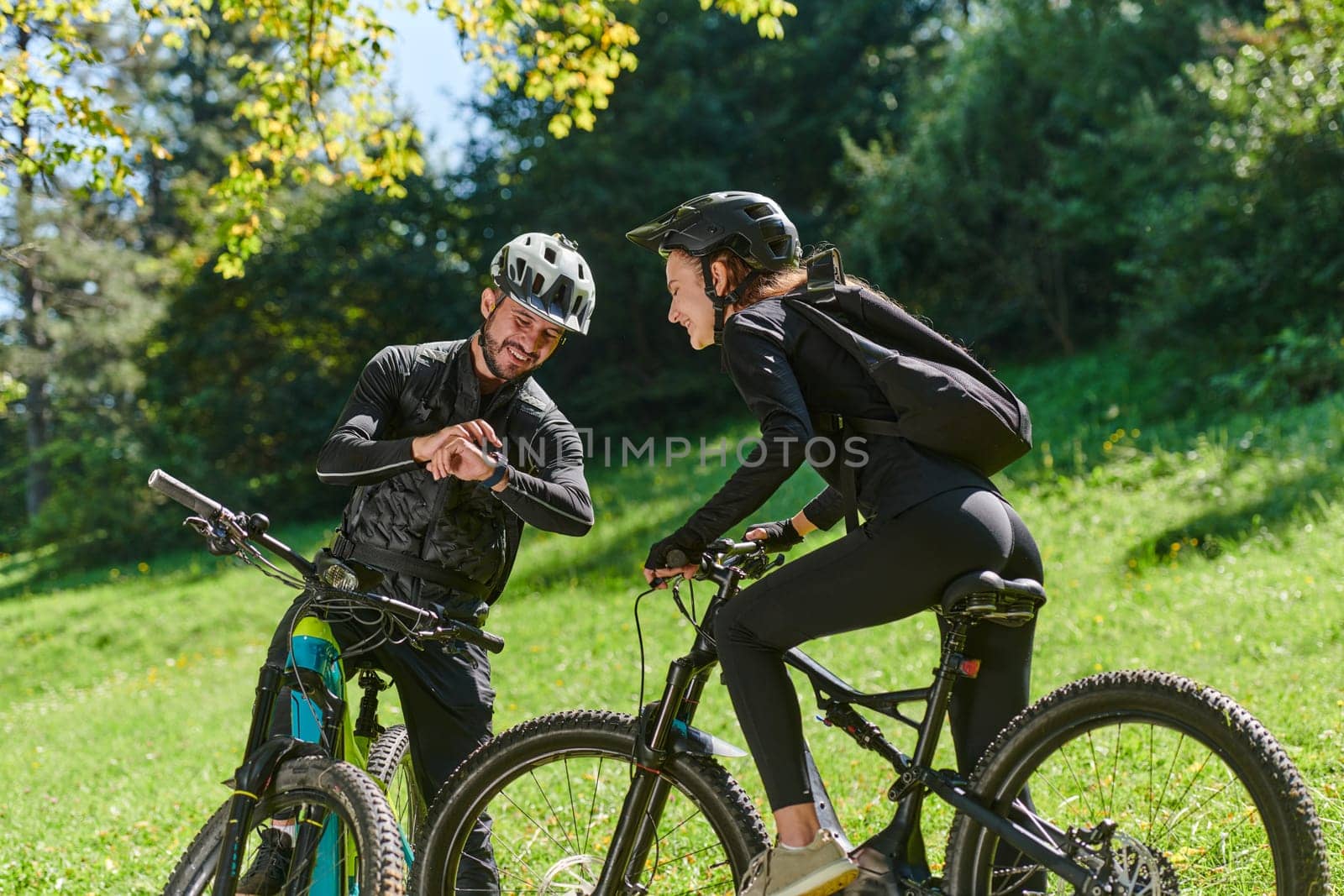 A sweet couple, equipped with bicycles and engrossed in coordinating their journey, checks their GPS mobile and watches while planning scenic routes in the park, seamlessly blending technology and outdoor adventure for a delightful cycling experience by dotshock