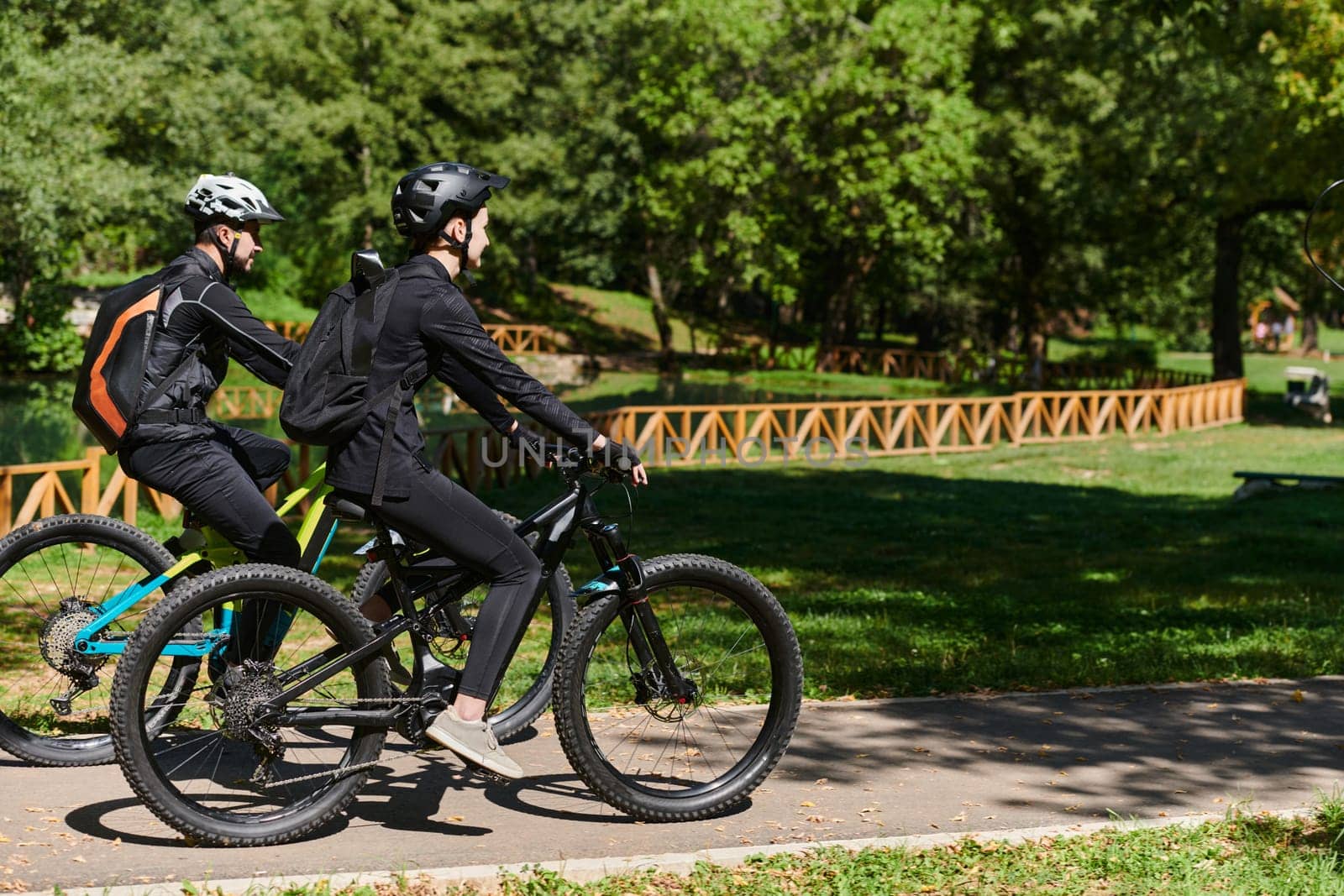 A blissful couple, adorned in professional cycling gear, enjoys a romantic bicycle ride through a park, surrounded by modern natural attractions, radiating love and happiness.