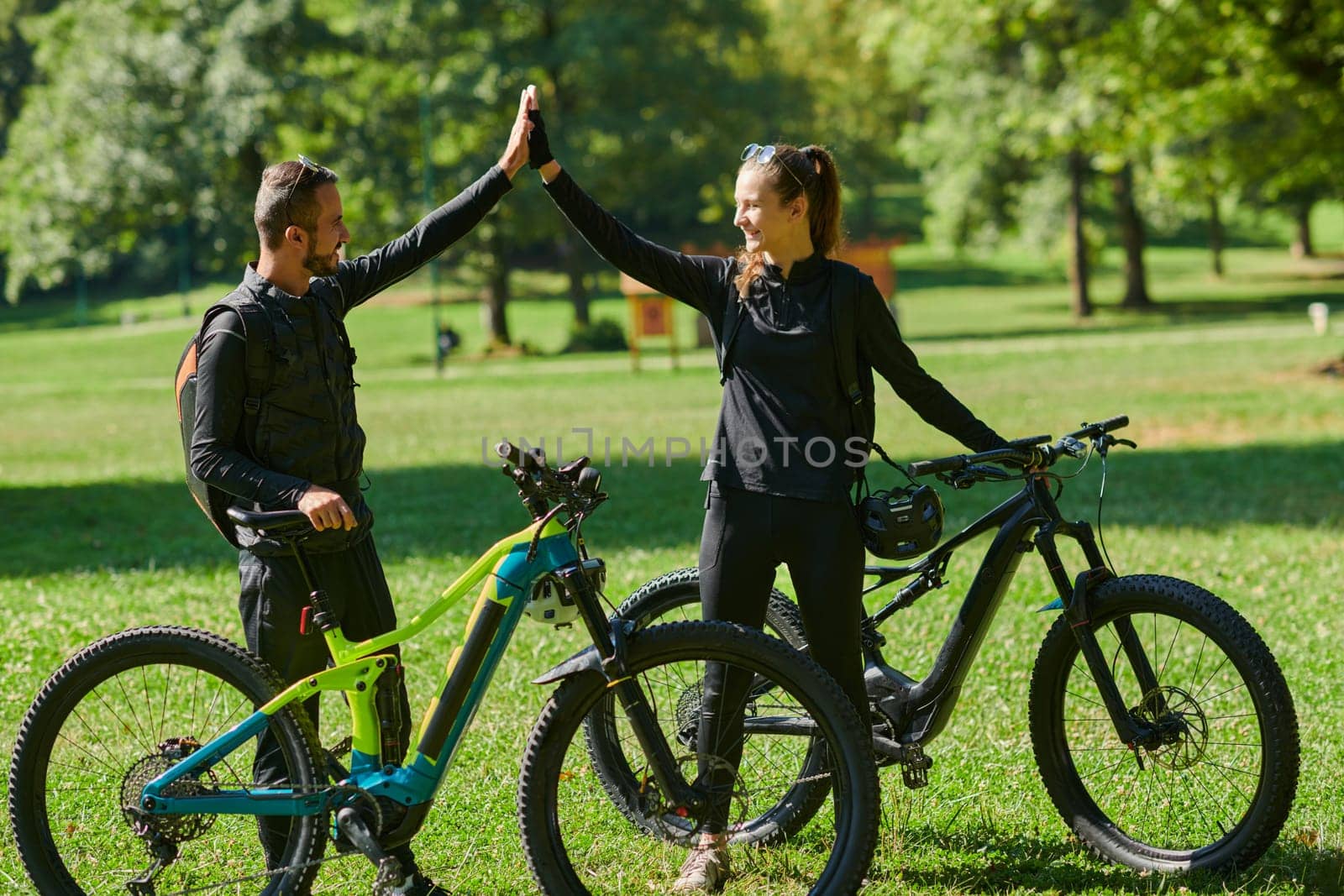 A sweet couple, adorned in cycling gear, rides their bicycles, their hands interlocked in a romantic embrace, capturing the essence of love, adventure, and joy on a sunlit path by dotshock