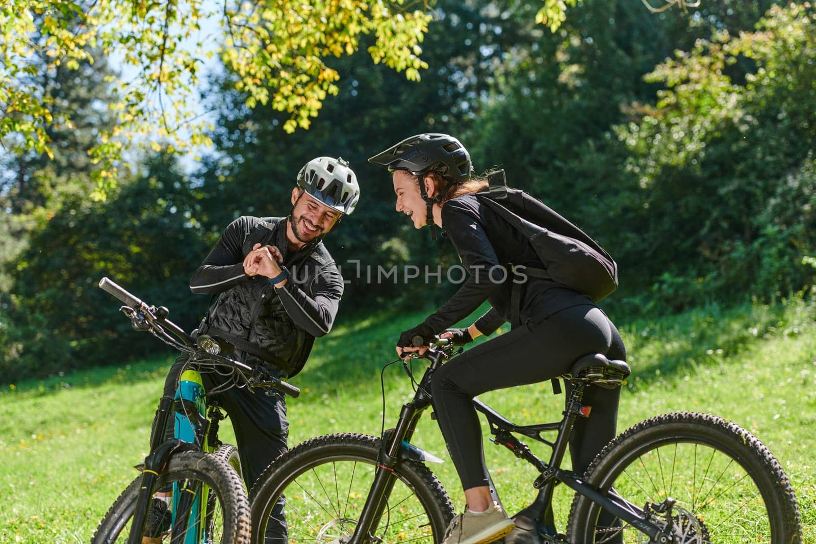 A sweet couple, equipped with bicycles and engrossed in coordinating their journey, checks their GPS mobile and watches while planning scenic routes in the park, seamlessly blending technology and outdoor adventure for a delightful cycling experience by dotshock