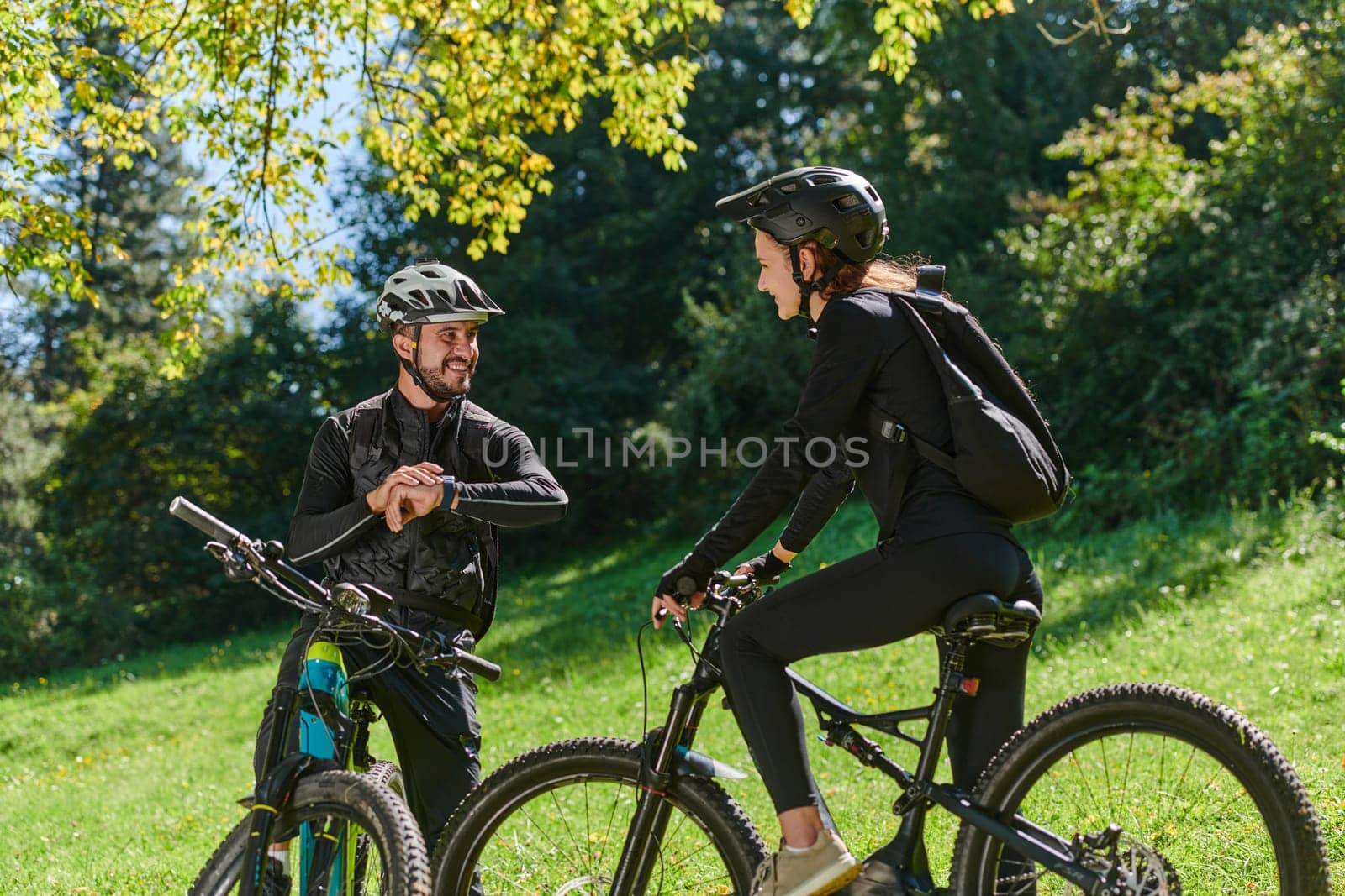 A sweet couple, equipped with bicycles and engrossed in coordinating their journey, checks their GPS mobile and watches while planning scenic routes in the park, seamlessly blending technology and outdoor adventure for a delightful cycling experience by dotshock