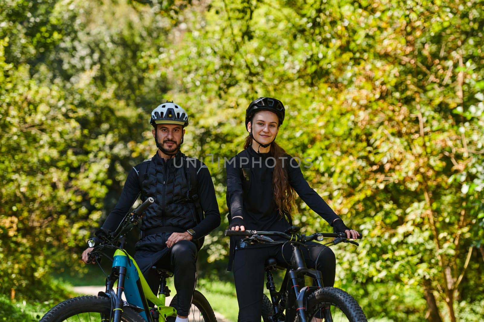 A blissful couple, adorned in professional cycling gear, enjoys a romantic bicycle ride through a park, surrounded by modern natural attractions, radiating love and happiness.