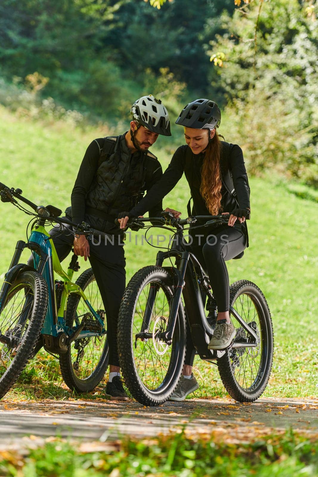 A sweet couple, equipped with bicycles and engrossed in coordinating their journey, checks their GPS mobile and watches while planning scenic routes in the park, seamlessly blending technology and outdoor adventure for a delightful cycling experience by dotshock