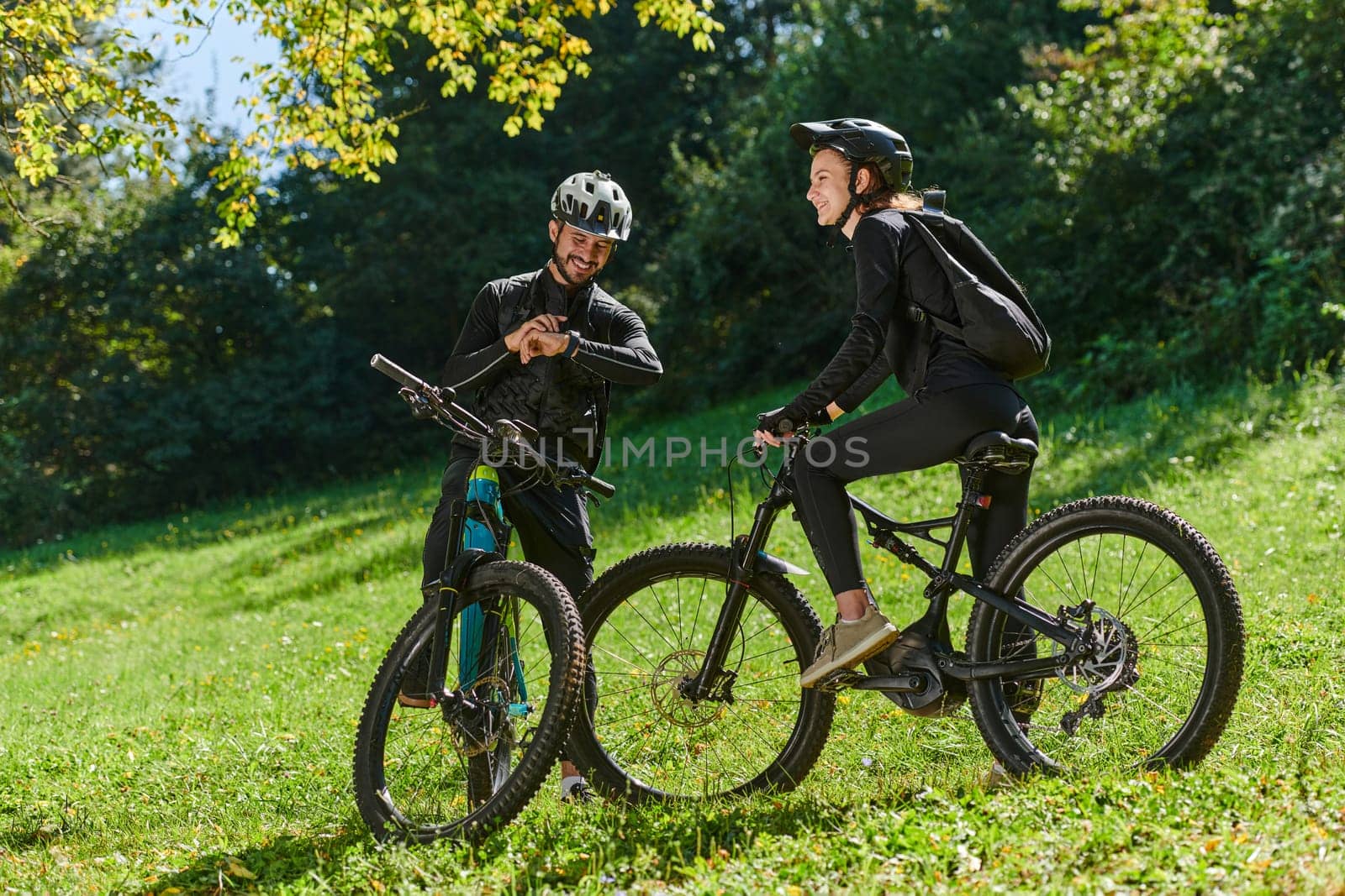 A sweet couple, equipped with bicycles and engrossed in coordinating their journey, checks their GPS mobile and watches while planning scenic routes in the park, seamlessly blending technology and outdoor adventure for a delightful cycling experience by dotshock