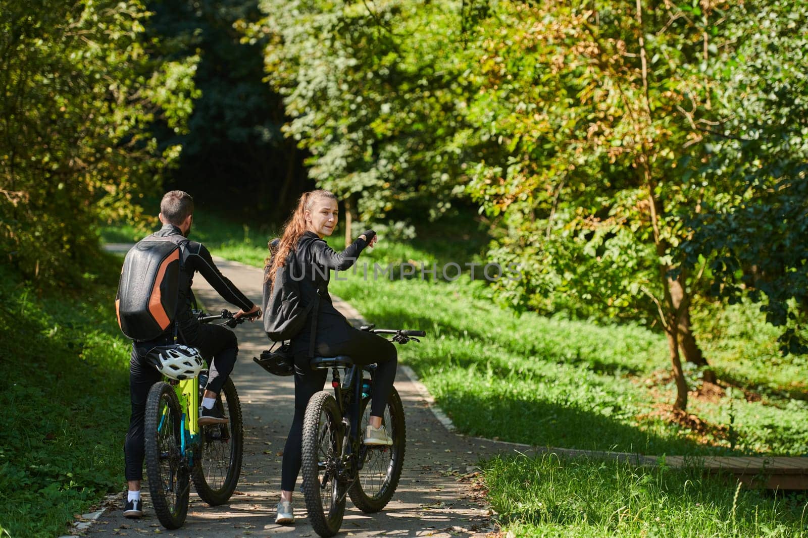 A blissful couple, adorned in professional cycling gear, enjoys a romantic bicycle ride through a park, surrounded by modern natural attractions, radiating love and happiness by dotshock