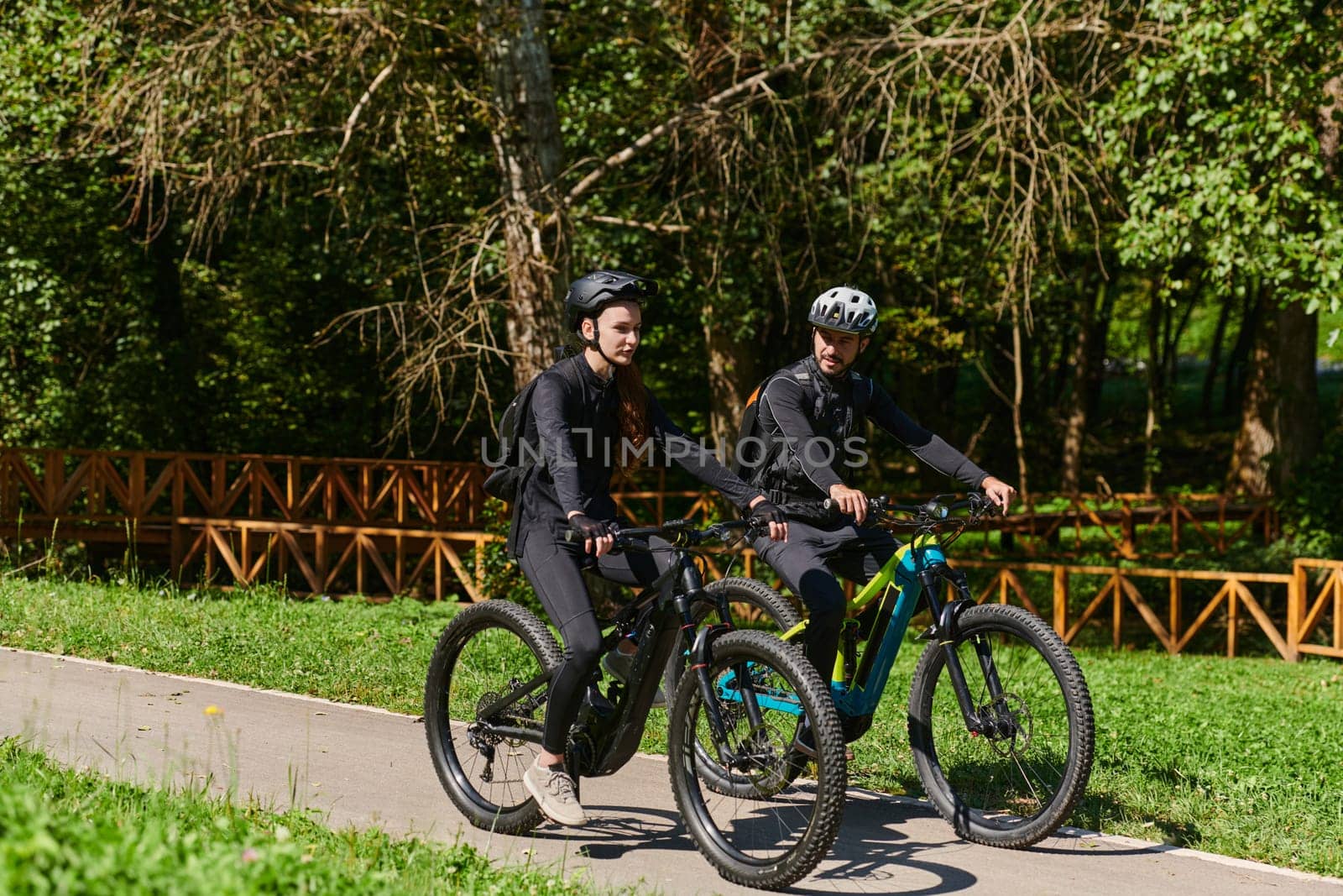 A blissful couple, adorned in professional cycling gear, enjoys a romantic bicycle ride through a park, surrounded by modern natural attractions, radiating love and happiness.