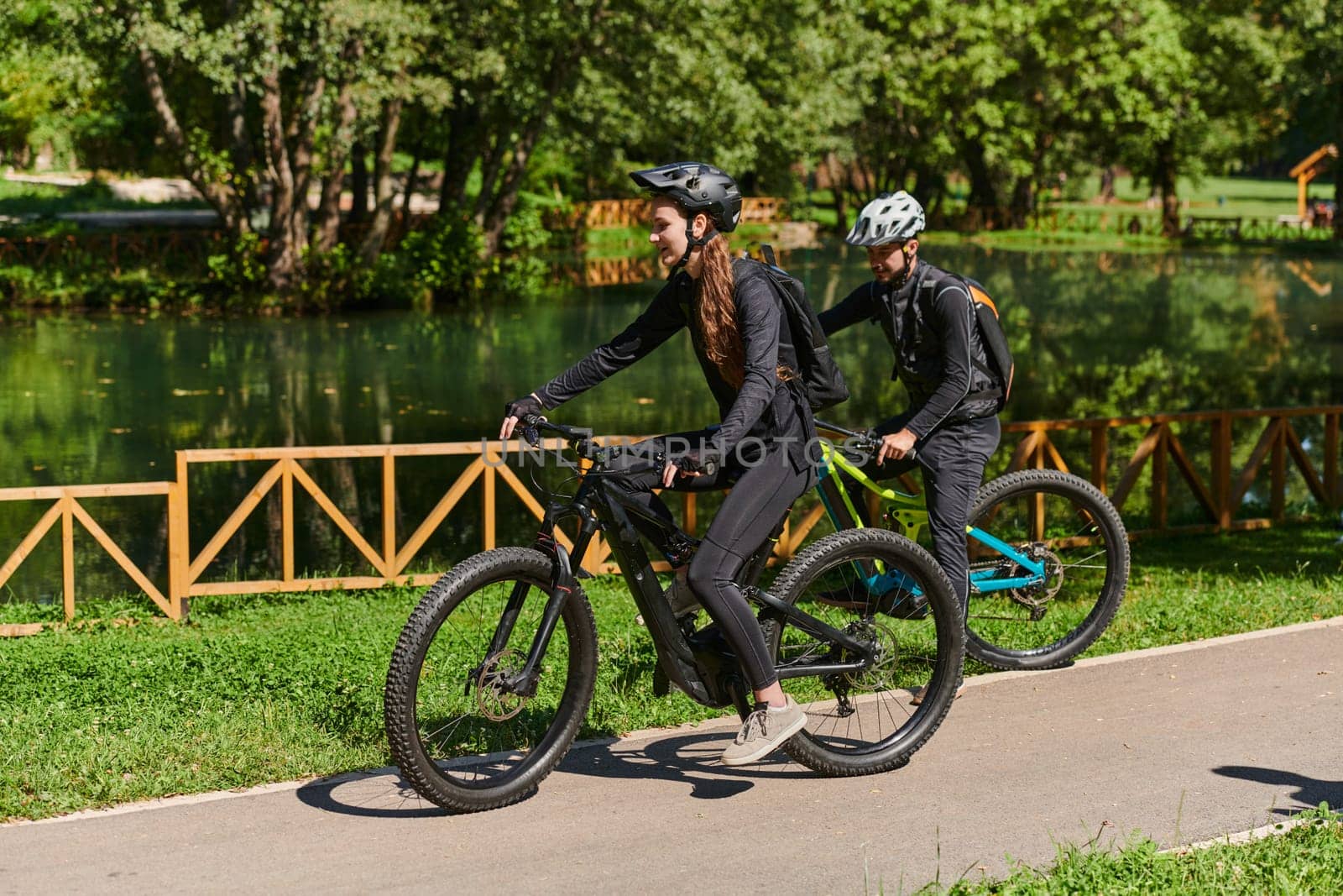 A blissful couple, adorned in professional cycling gear, enjoys a romantic bicycle ride through a park, surrounded by modern natural attractions, radiating love and happiness.