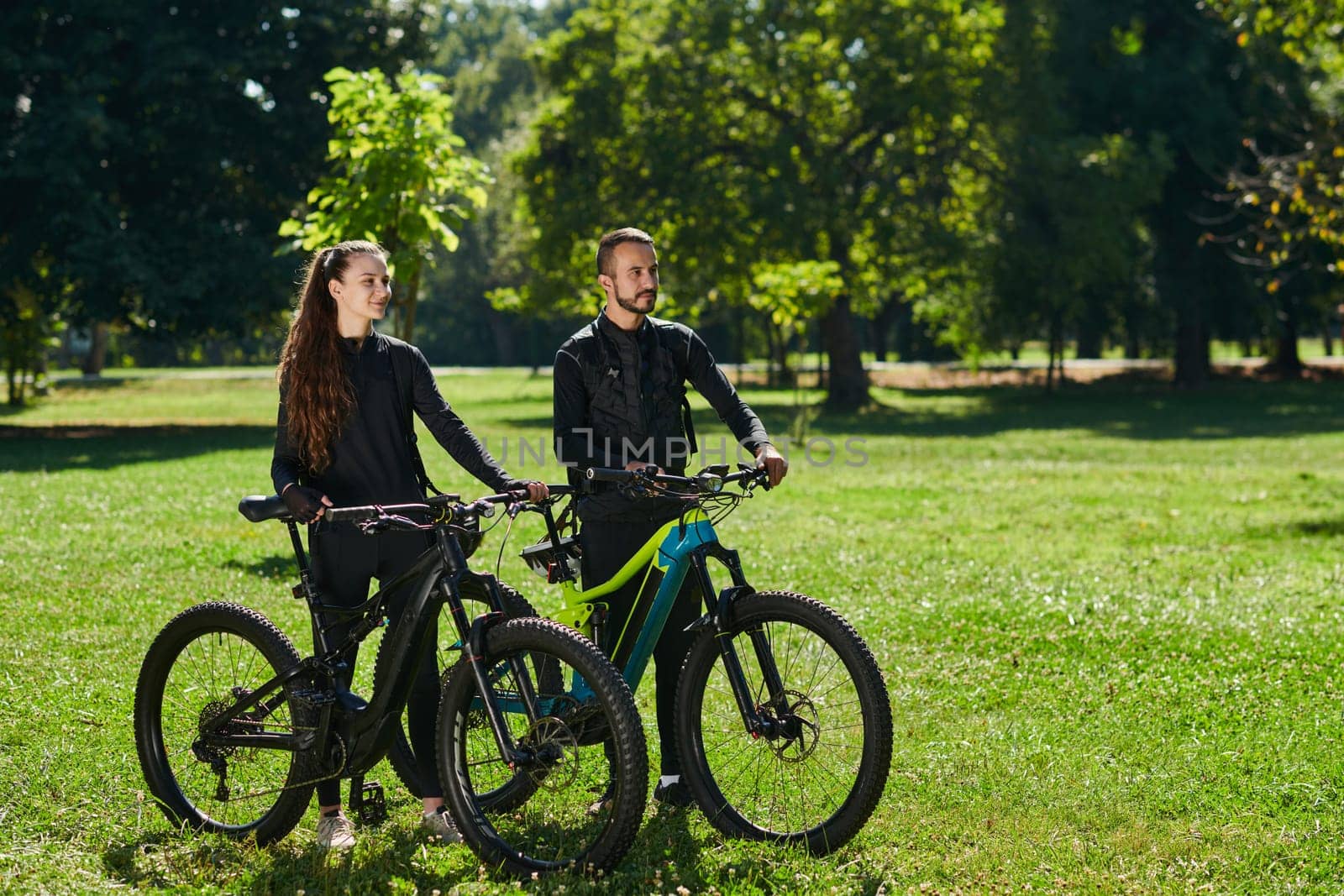 A blissful couple, adorned in professional cycling gear, enjoys a romantic bicycle ride through a park, surrounded by modern natural attractions, radiating love and happiness by dotshock