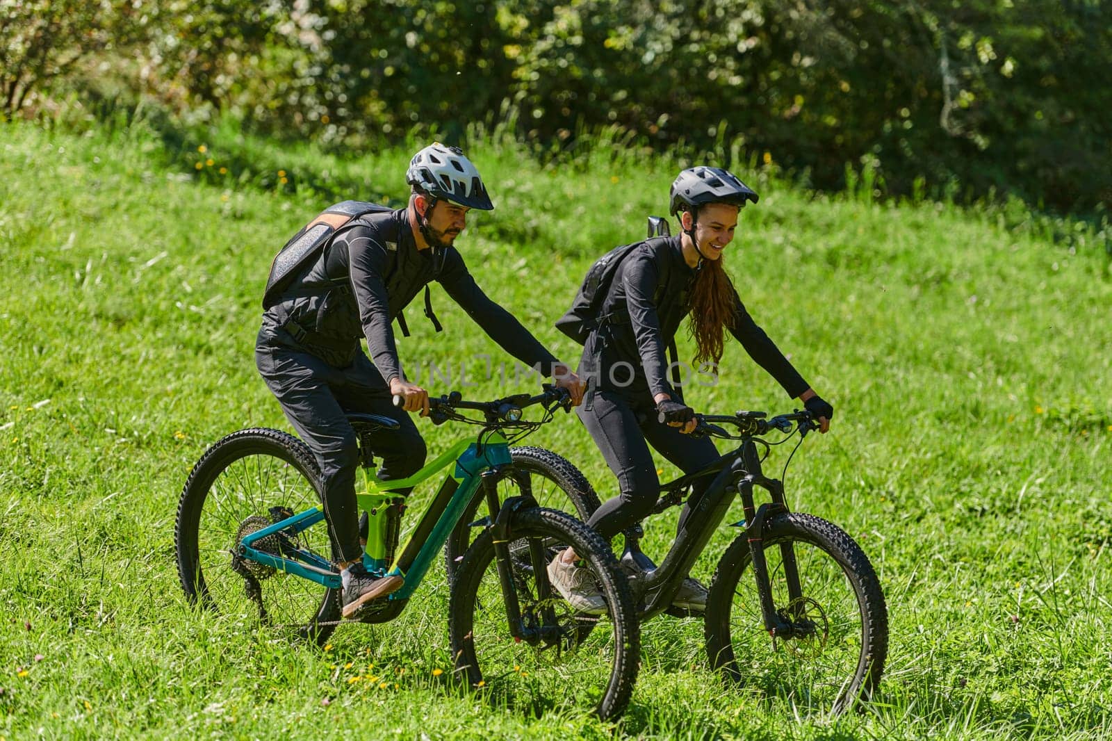 A blissful couple, adorned in professional cycling gear, enjoys a romantic bicycle ride through a park, surrounded by modern natural attractions, radiating love and happiness by dotshock