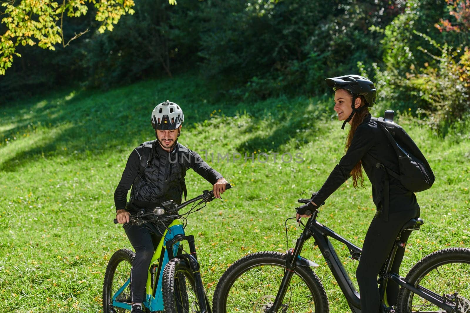 A blissful couple, adorned in professional cycling gear, enjoys a romantic bicycle ride through a park, surrounded by modern natural attractions, radiating love and happiness.