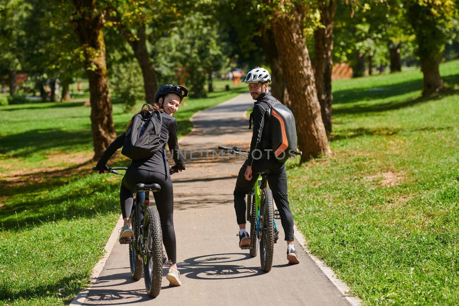 A blissful couple, adorned in professional cycling gear, enjoys a romantic bicycle ride through a park, surrounded by modern natural attractions, radiating love and happiness.