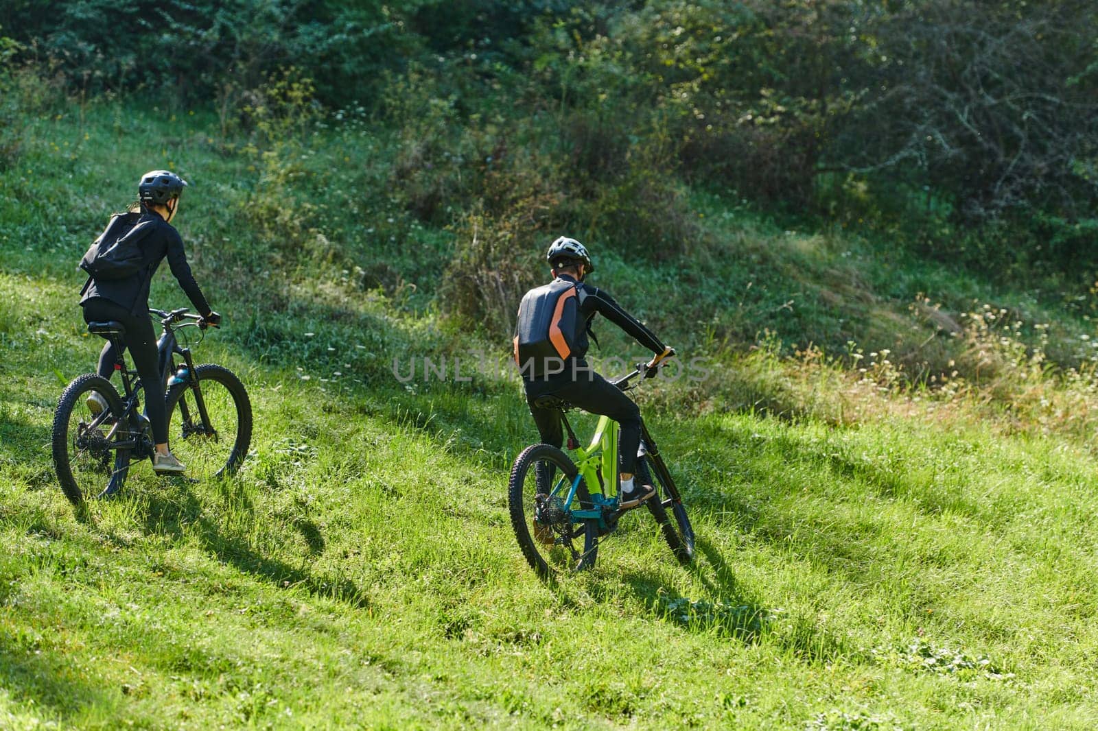 A blissful couple, adorned in professional cycling gear, enjoys a romantic bicycle ride through a park, surrounded by modern natural attractions, radiating love and happiness by dotshock