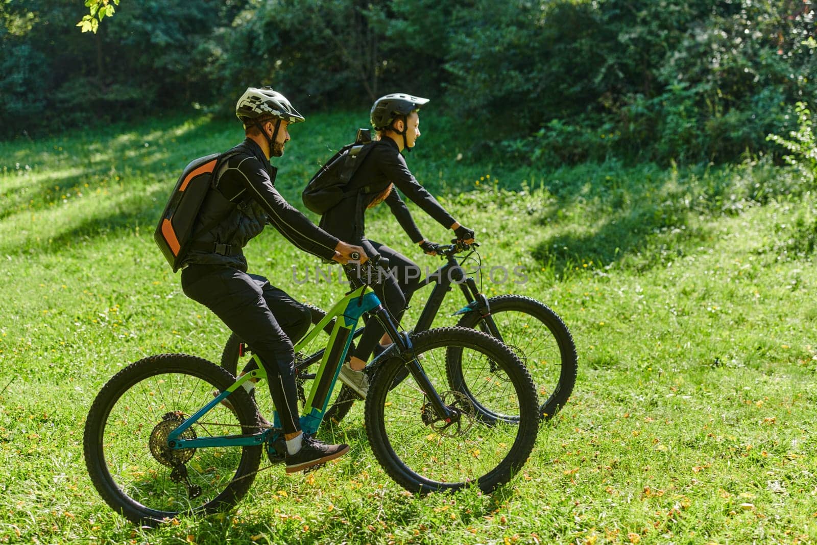 A blissful couple, adorned in professional cycling gear, enjoys a romantic bicycle ride through a park, surrounded by modern natural attractions, radiating love and happiness.