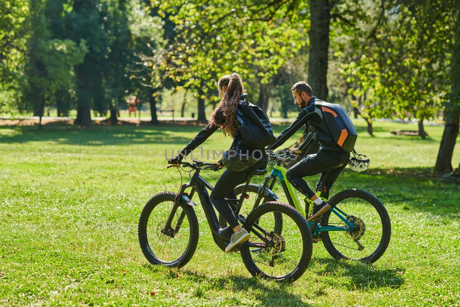 A blissful couple, adorned in professional cycling gear, enjoys a romantic bicycle ride through a park, surrounded by modern natural attractions, radiating love and happiness.