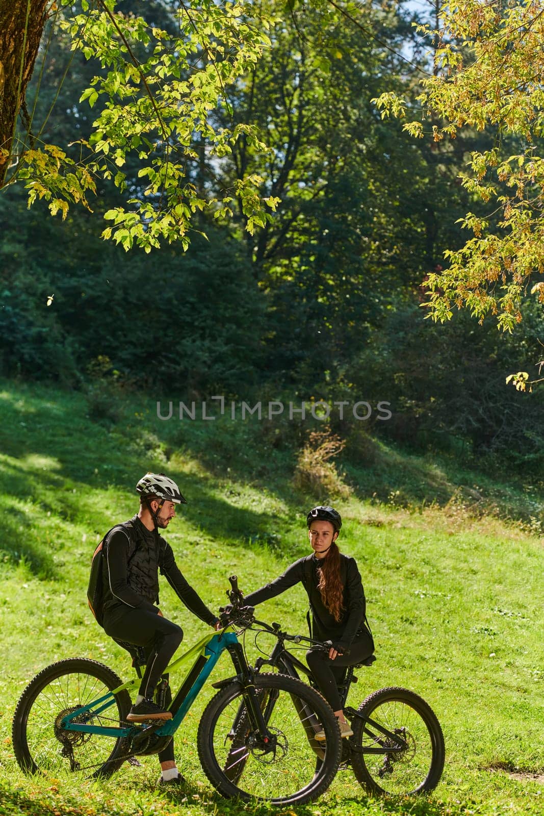 A sweet couple, equipped with bicycles and engrossed in coordinating their journey, checks their GPS mobile and watches while planning scenic routes in the park, seamlessly blending technology and outdoor adventure for a delightful cycling experience by dotshock