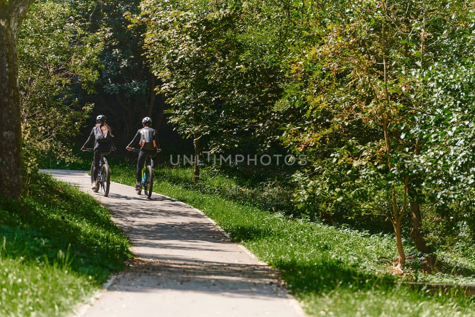 A blissful couple, adorned in professional cycling gear, enjoys a romantic bicycle ride through a park, surrounded by modern natural attractions, radiating love and happiness.