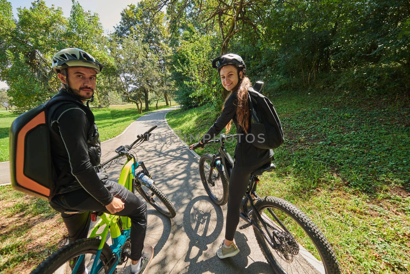 A sweet couple, adorned in cycling gear, rides their bicycles, their hands interlocked in a romantic embrace, capturing the essence of love, adventure, and joy on a sunlit path by dotshock