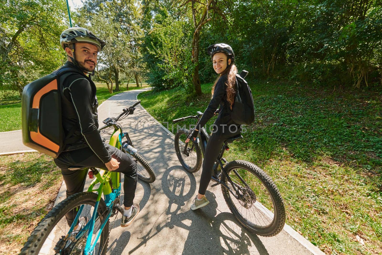 A sweet couple, adorned in cycling gear, rides their bicycles, their hands interlocked in a romantic embrace, capturing the essence of love, adventure, and joy on a sunlit path.