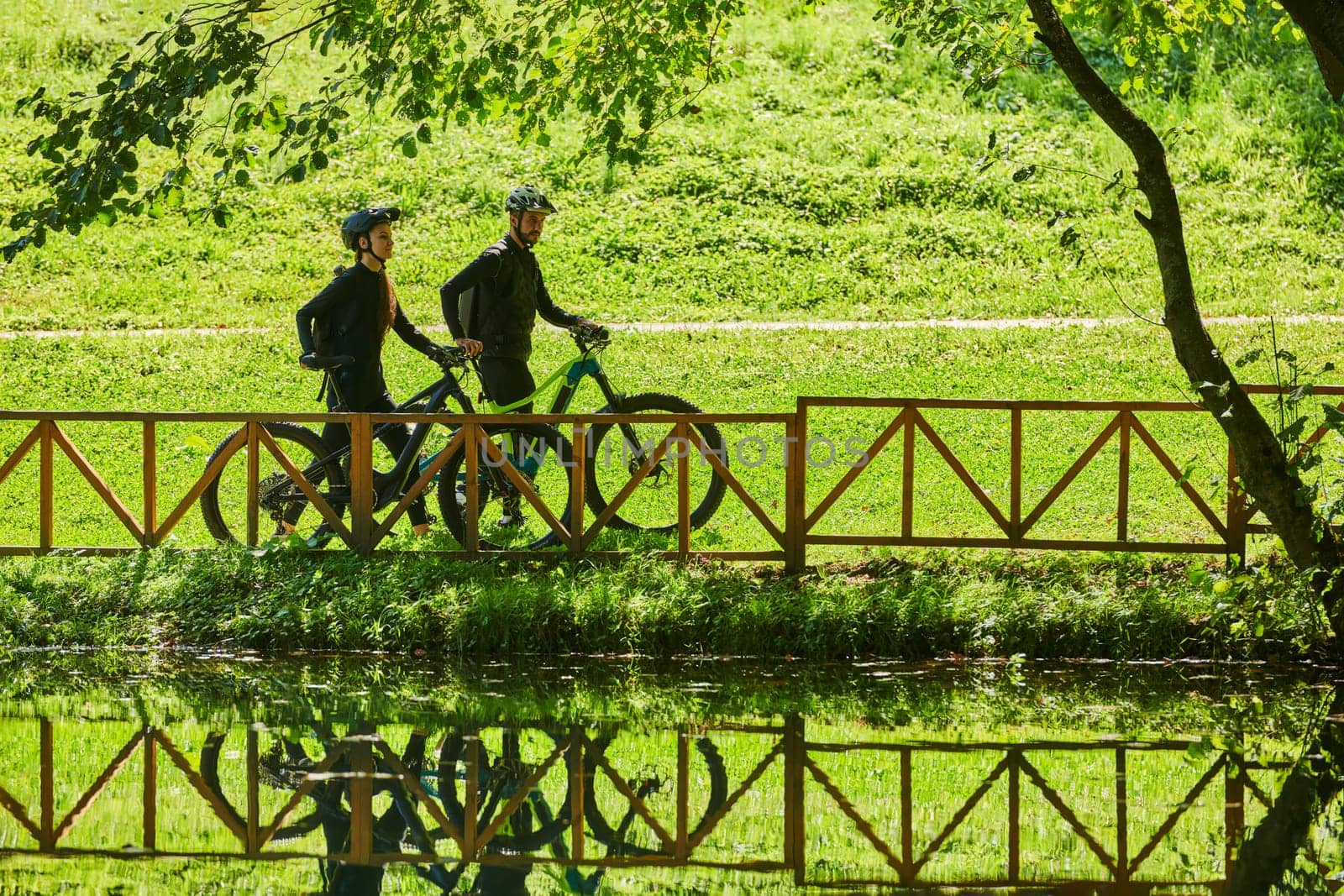 A blissful couple, adorned in professional cycling gear, enjoys a romantic bicycle ride through a park, surrounded by modern natural attractions, radiating love and happiness.